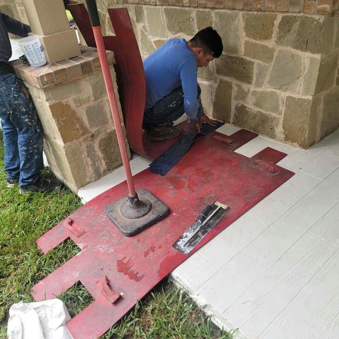 Worker kneeling, applying material to a white concrete surface, using a large red platform.