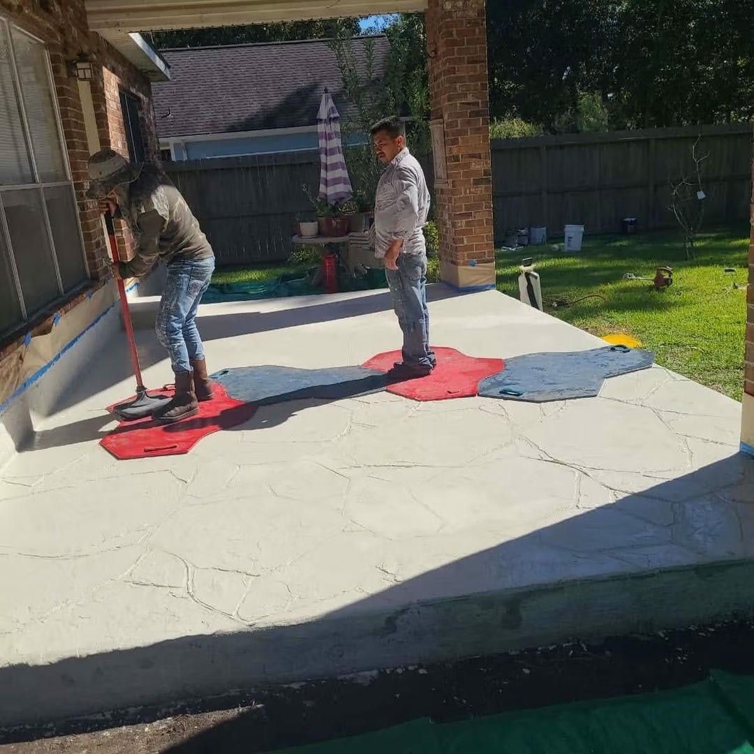 Two people applying concrete sealant on an outdoor patio.