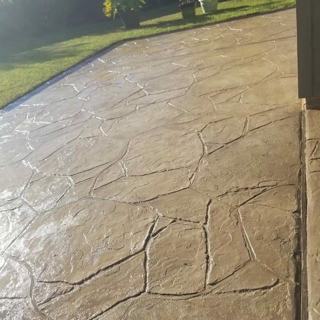 Person sealing a stamped concrete driveway, two-car garage in the background. Brown and reddish tones.