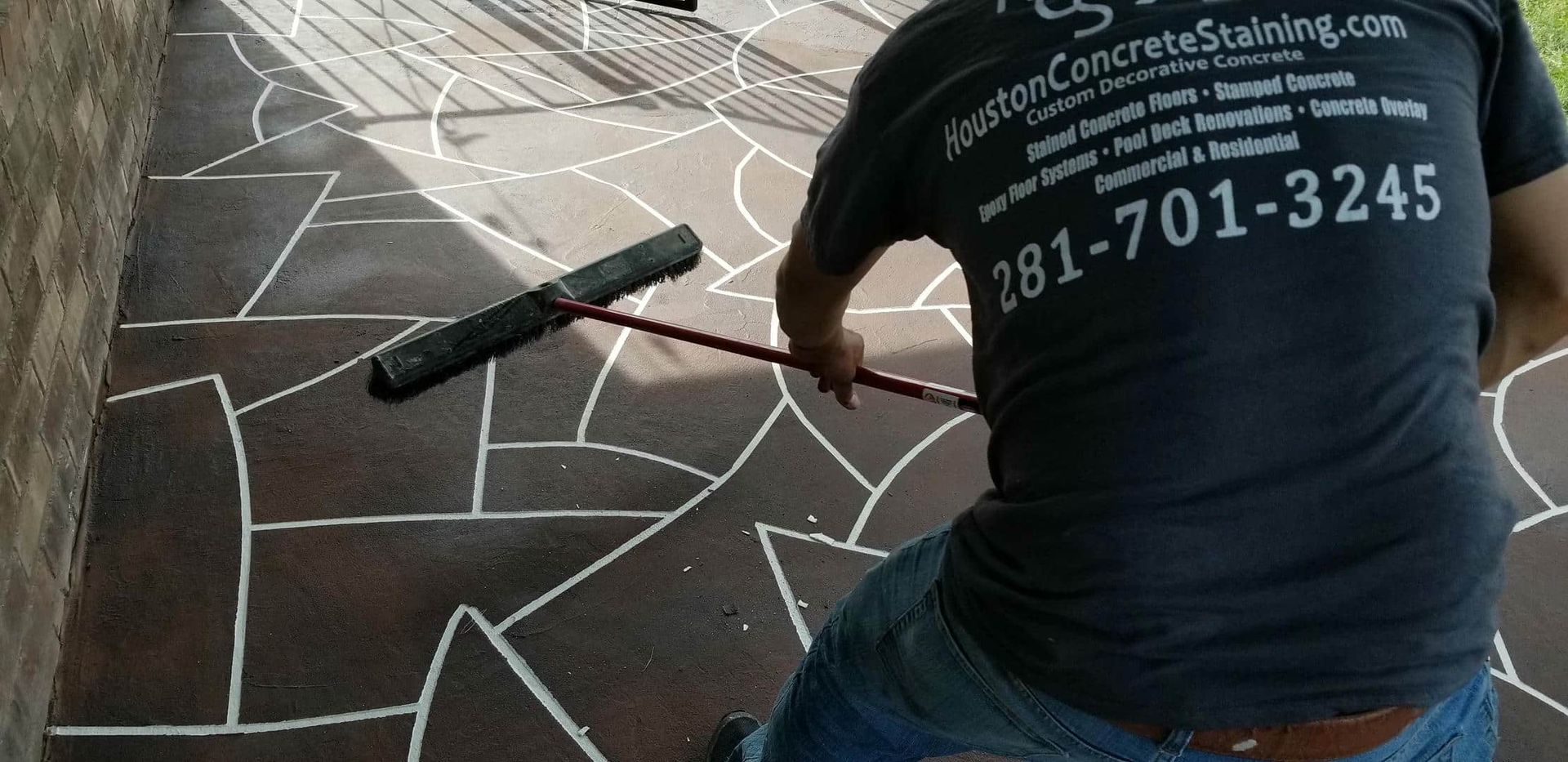 Person applying sealant to a decorative concrete surface, using a long-handled tool.