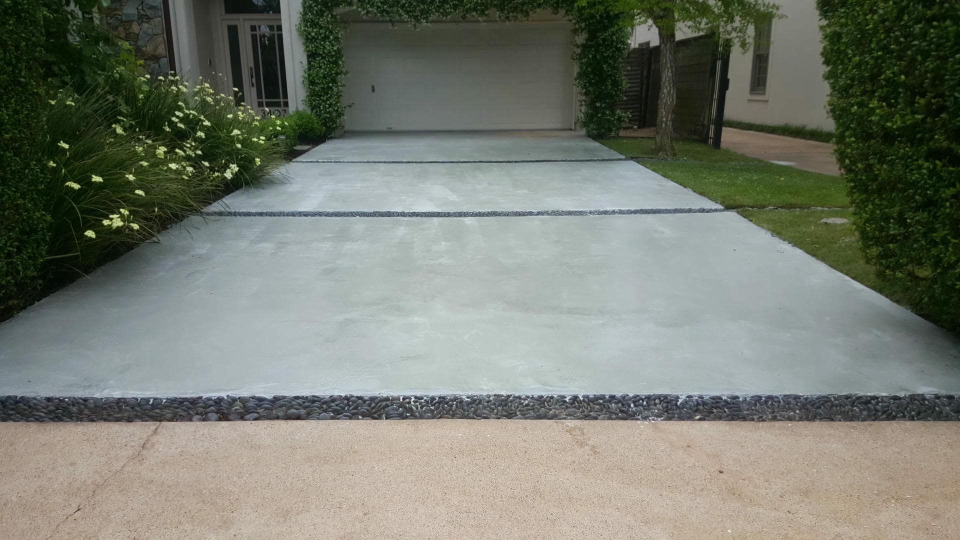 Concrete driveway leading to a garage, bordered by greenery.