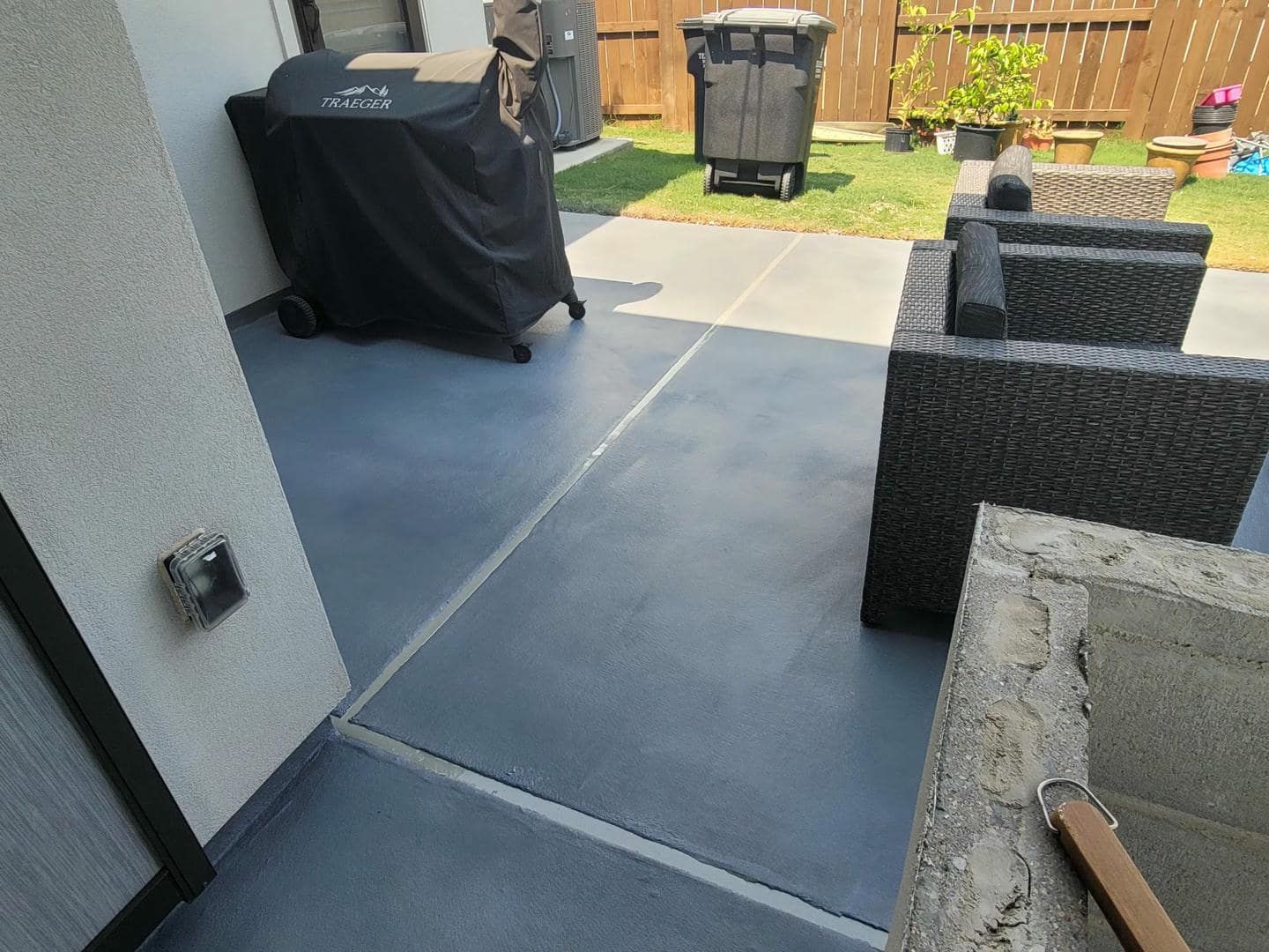 Outdoor patio with gray painted concrete, grill, black furniture, and trash cans.