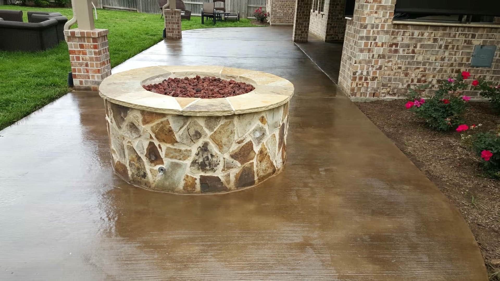 Outdoor patio with a stone fire pit and brown concrete flooring.