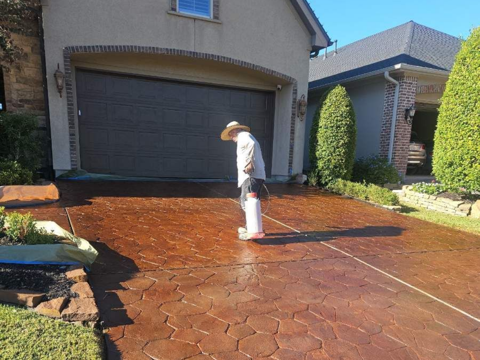 Person inspecting a newly stained brown concrete driveway in front of a house with a garage.