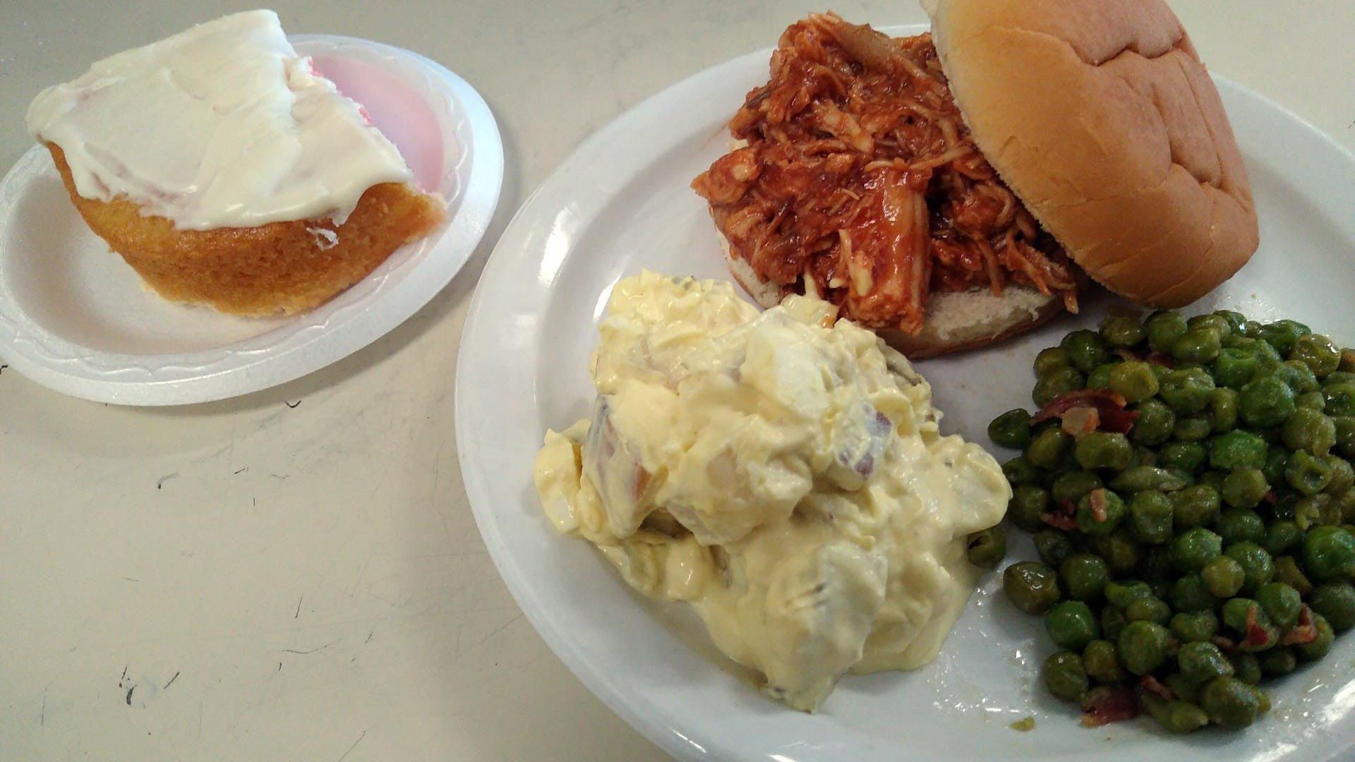 A plate of food with a sandwich , potato salad , and peas on a table.