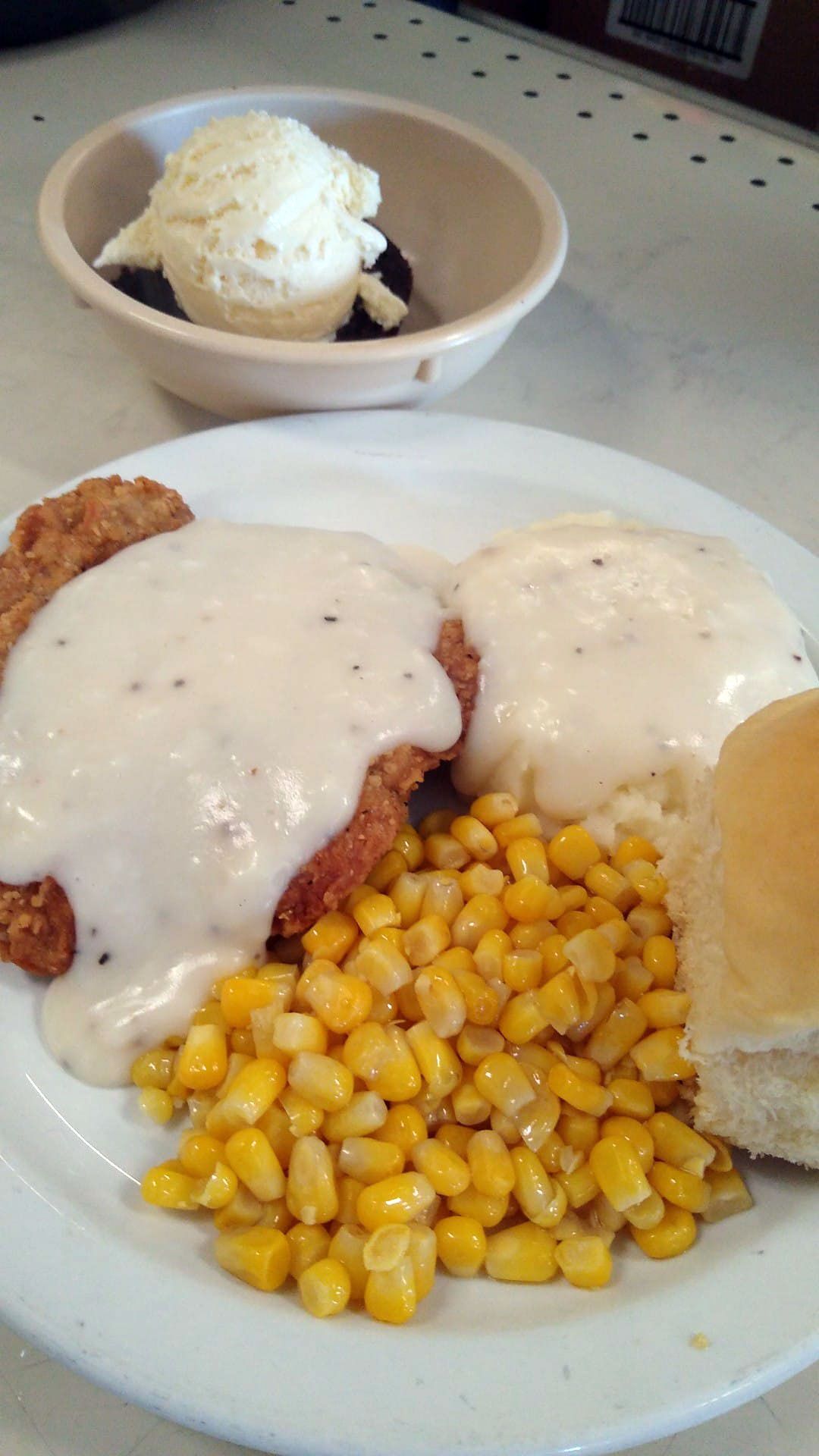 A plate of food with corn , biscuits and gravy on a table.