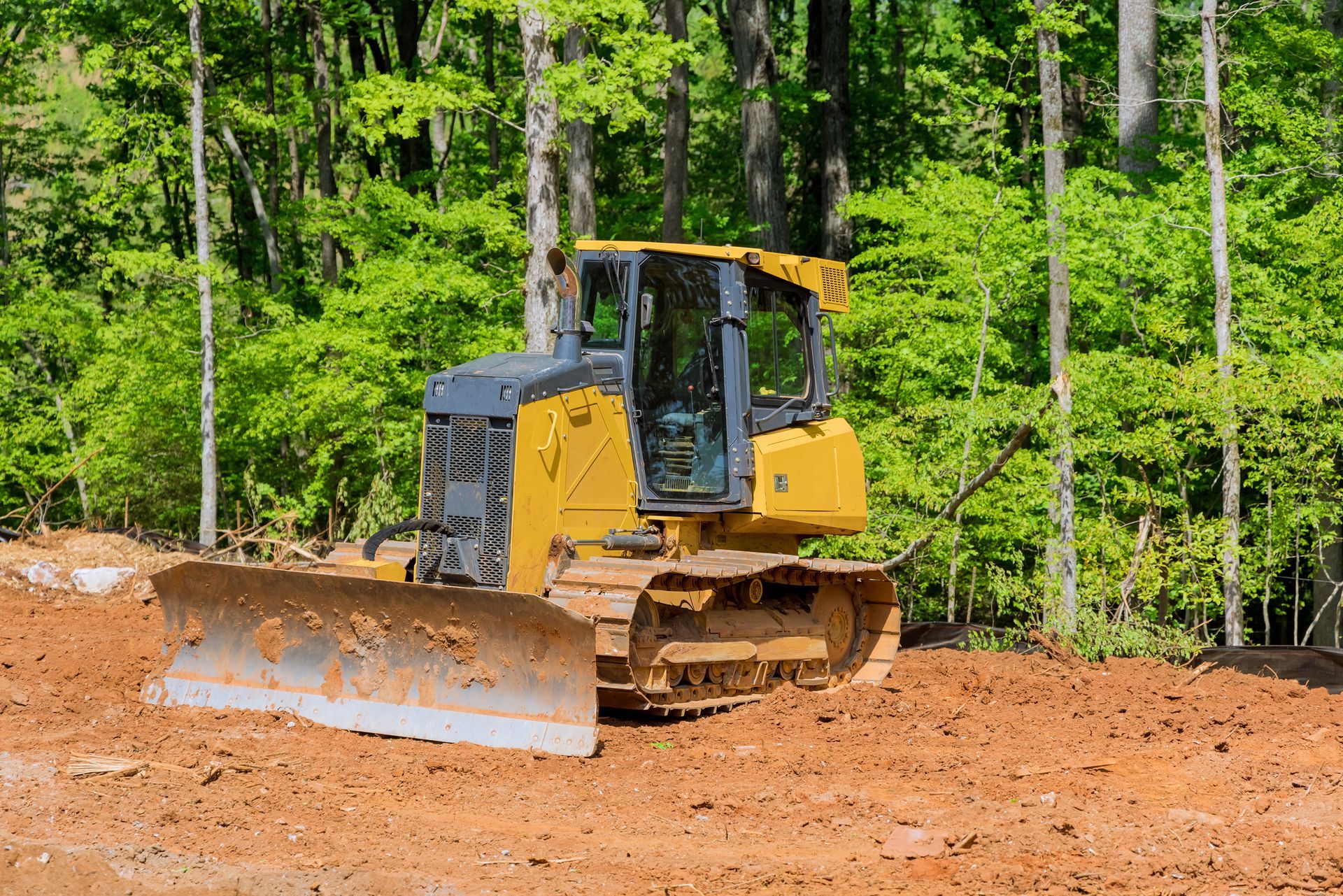 A bulldozer is moving dirt in a field in the woods.