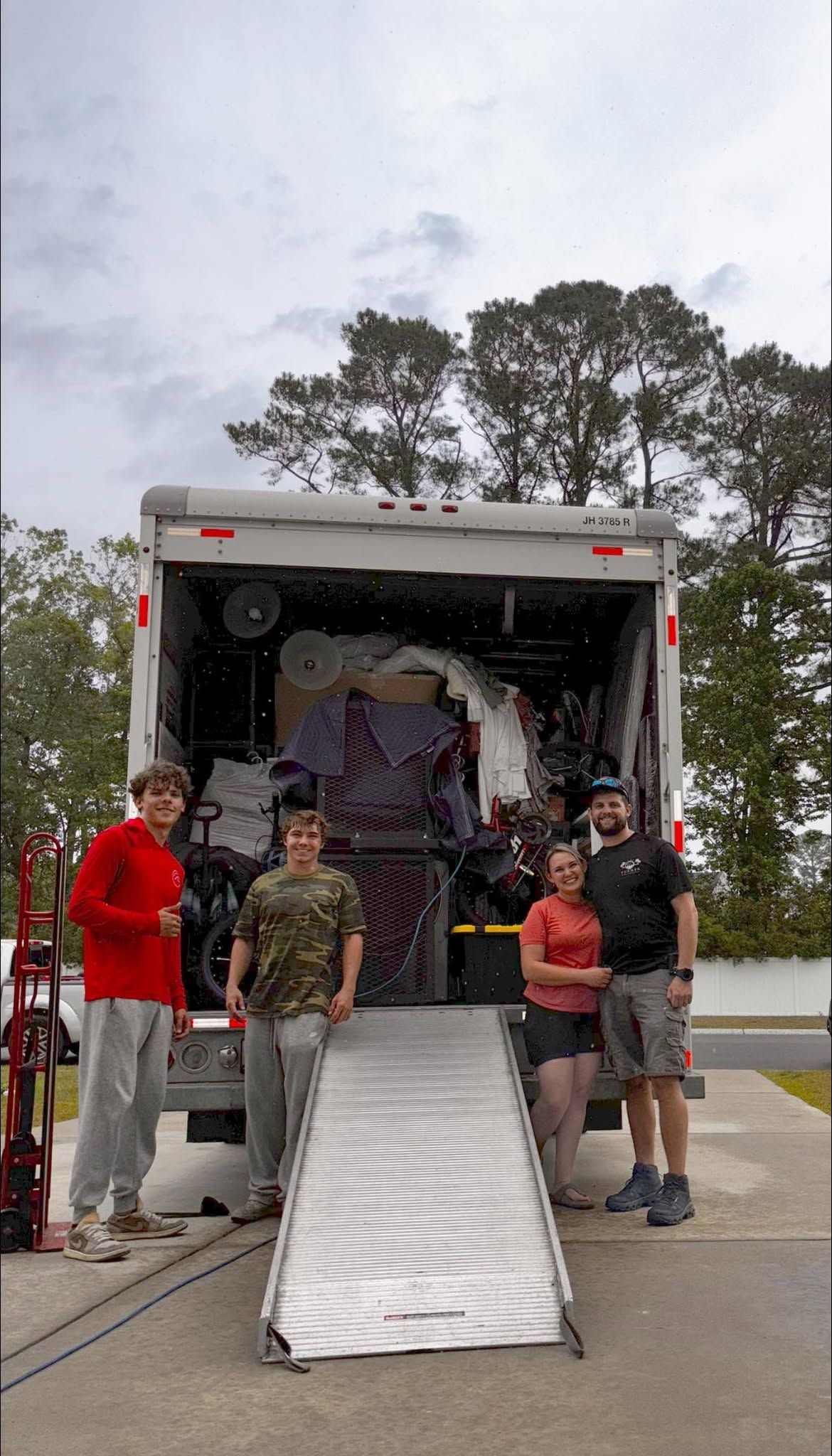 People posing beside a box truck with a metal ramp extended on a road.