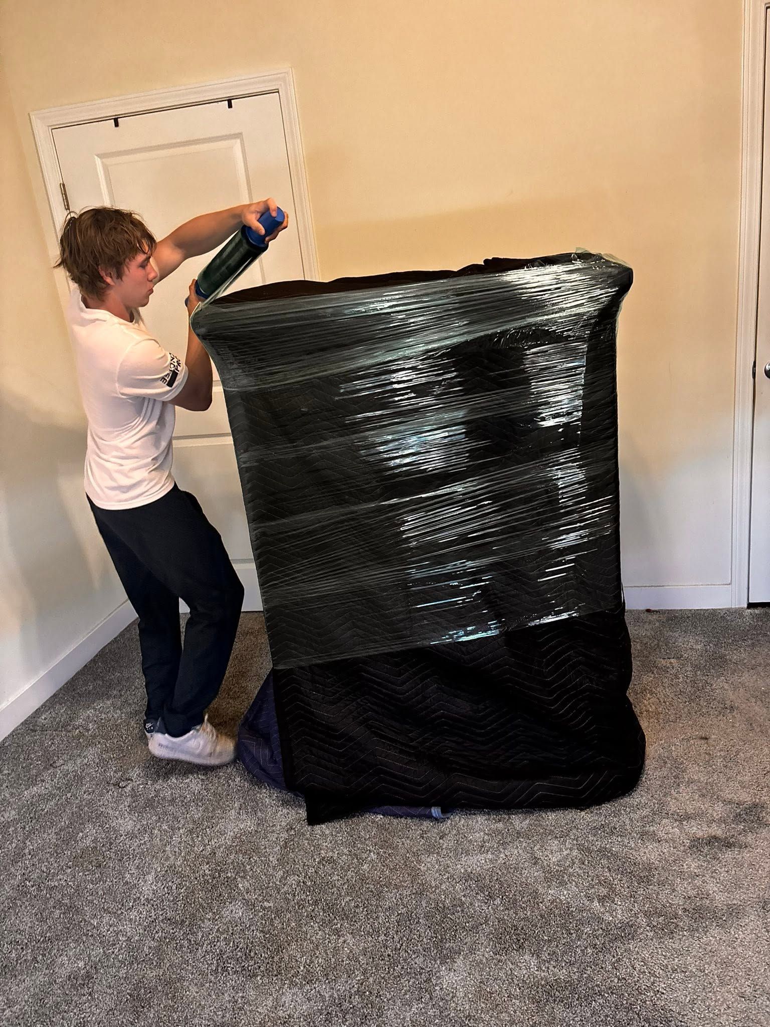 Person sealing a large black trash bag beside a white door in a carpeted room