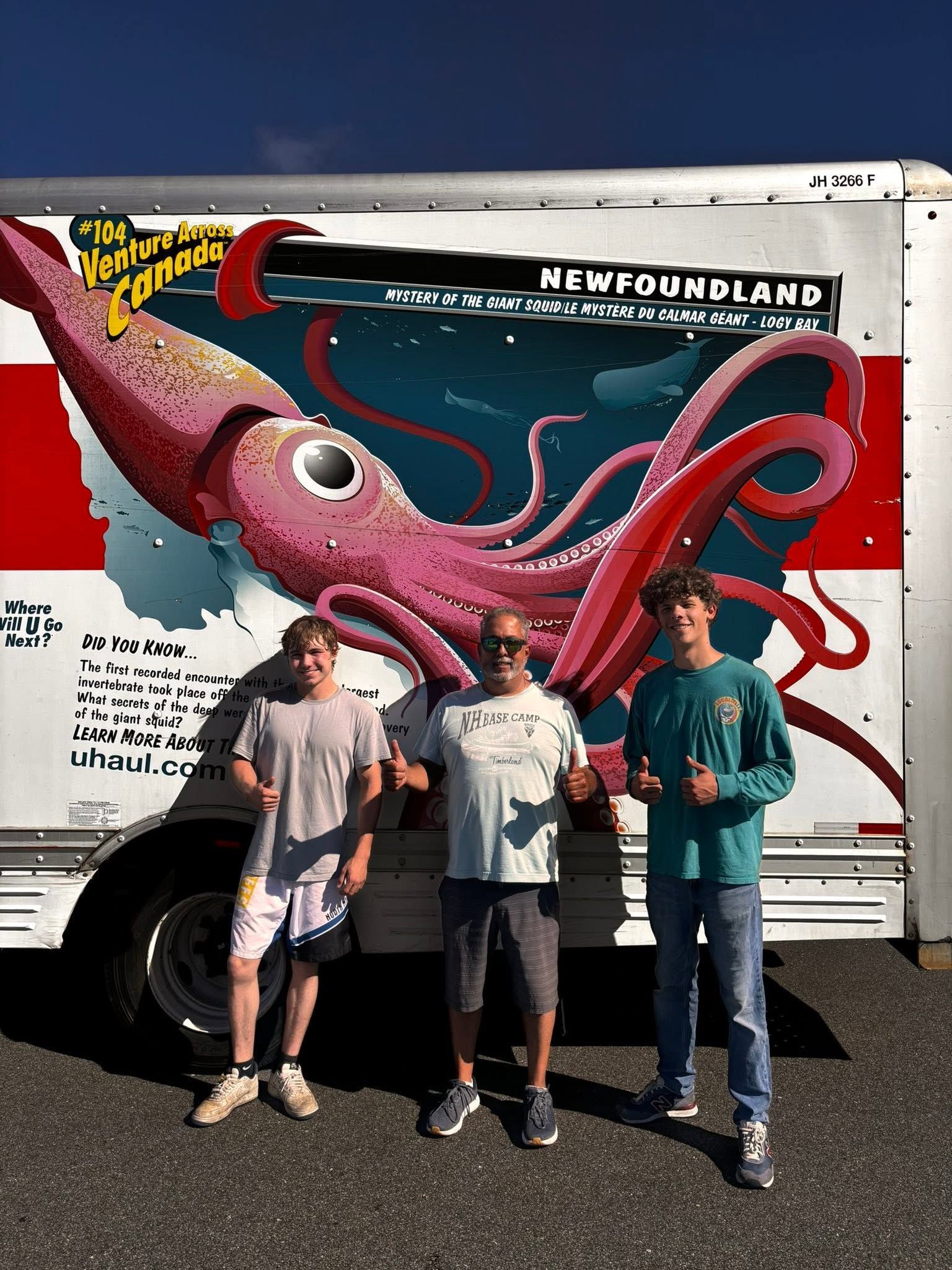 Three people posing before a colorful Newfie-themed truck mural with a large pink squid.
