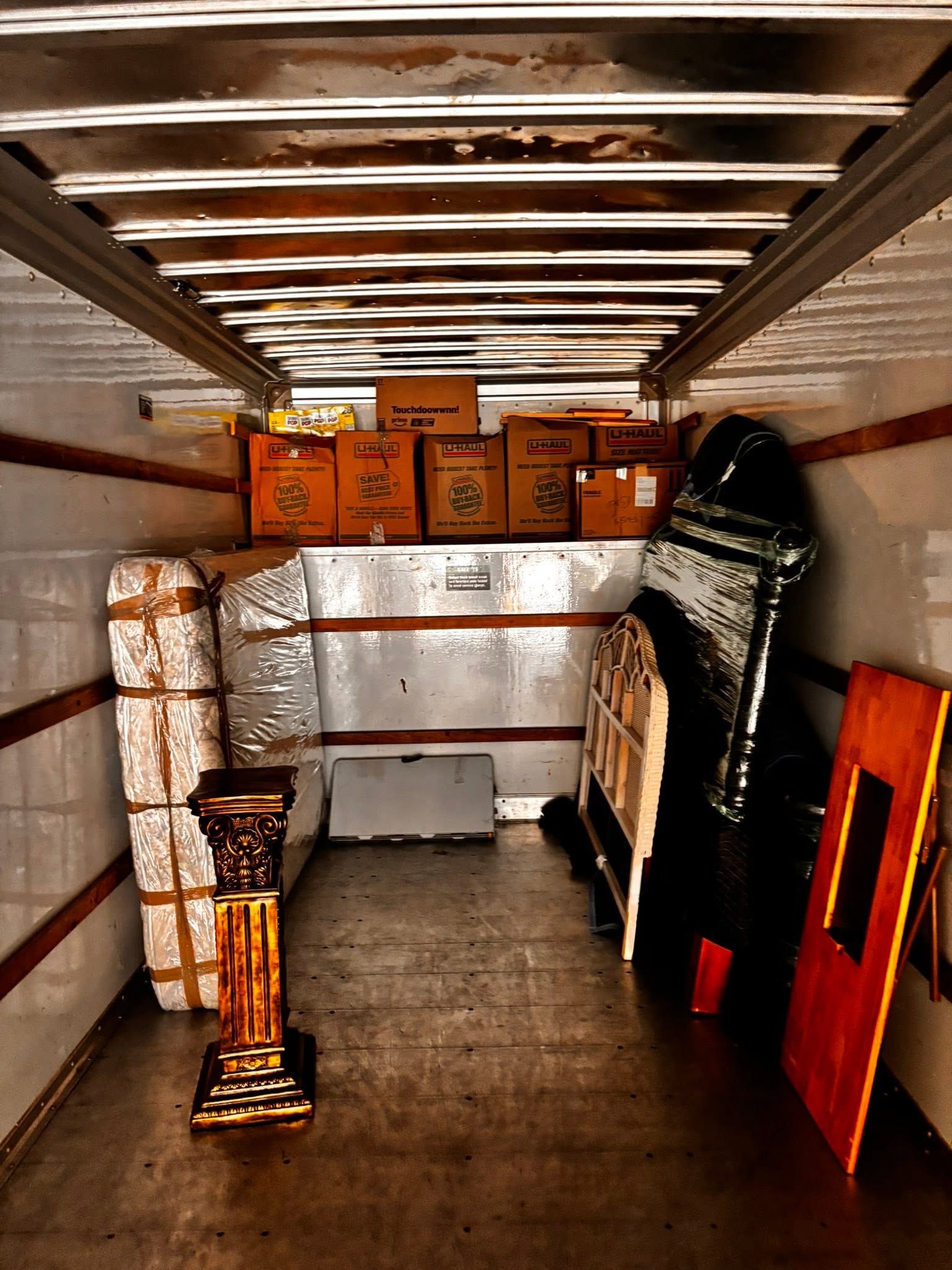 Inside a moving truck, stacked framed items and furniture are secured along the walls.