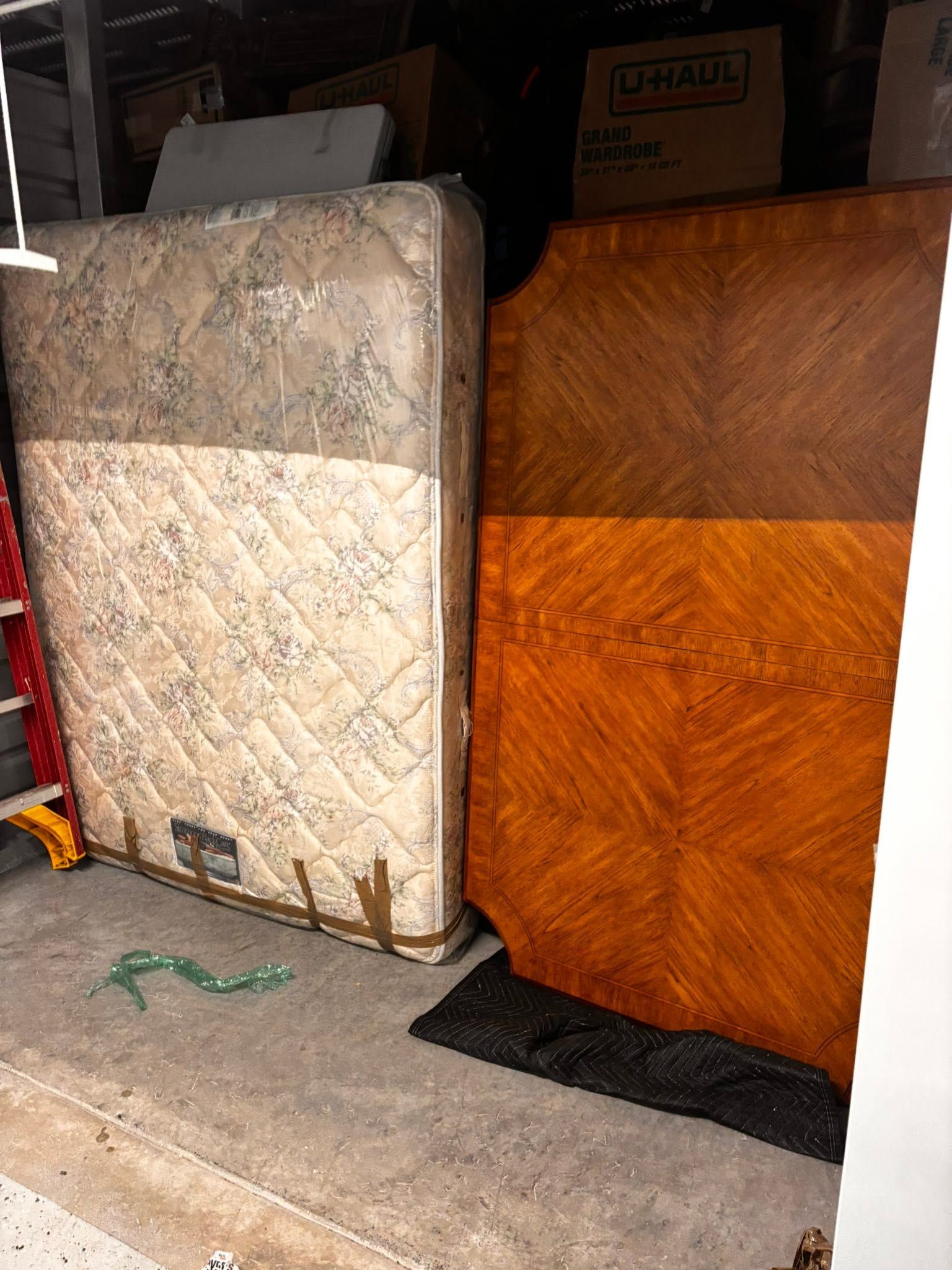 Two old mattresses leaning in a garage, one cream quilted and one orange wood-patterned.