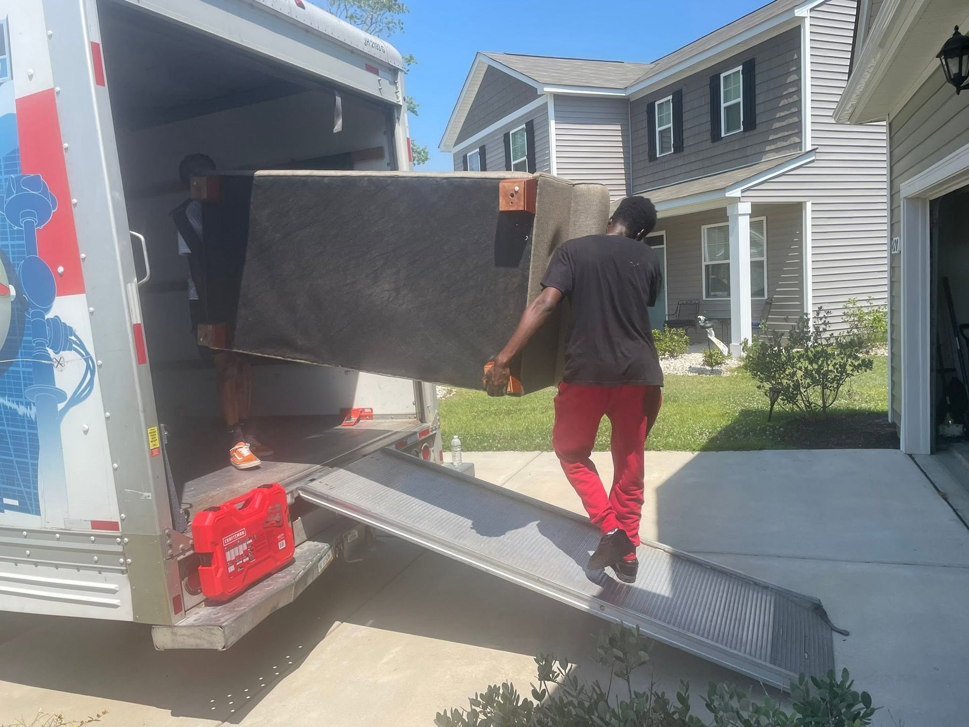 Movers loading a large black couch into a truck via a ramp outside a house