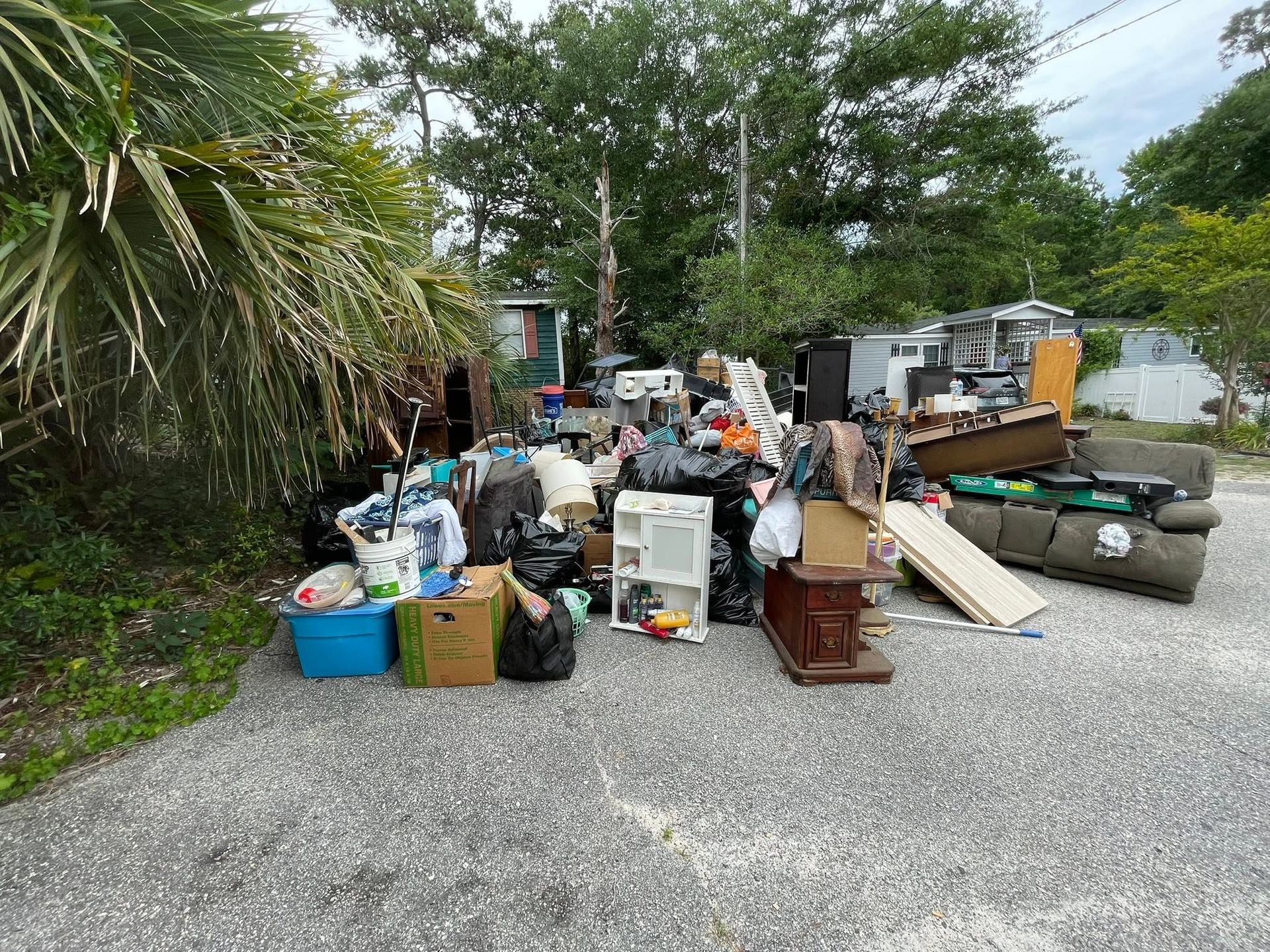 Outdoor pile of discarded furniture, appliances, and boxes on a gravel roadside near trees