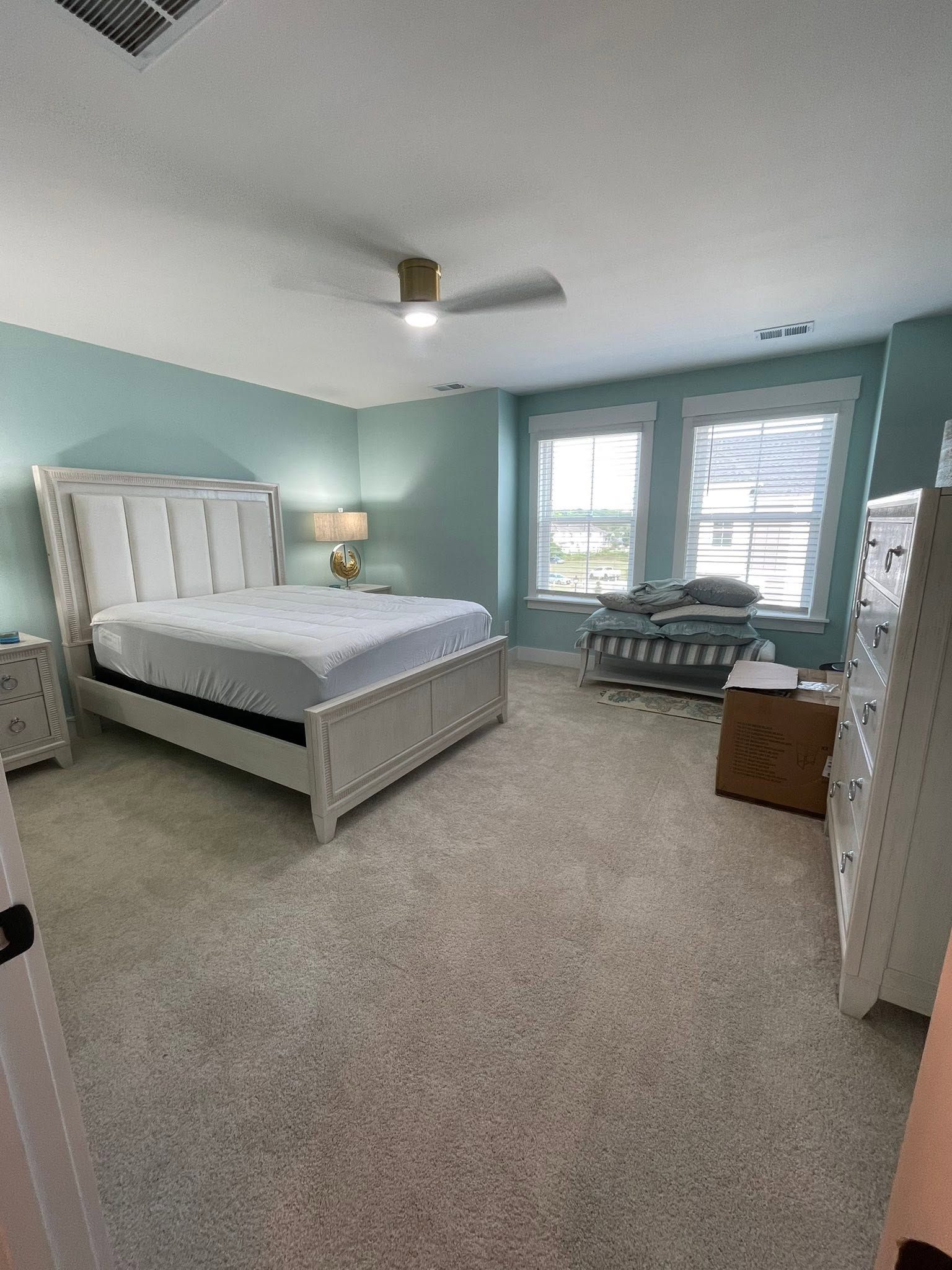 Bright bedroom with a white bed, teal walls, carpet, and a sitting area by large windows.