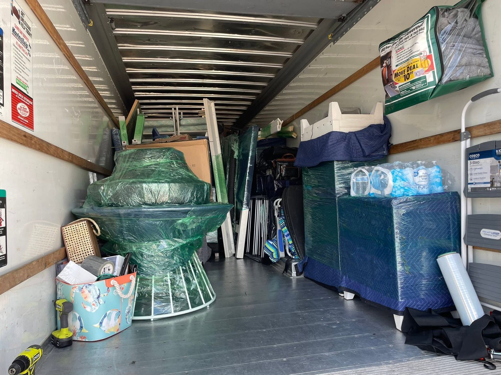 Packed moving truck interior with wrapped furniture, boxes, and stacked items along both sides.