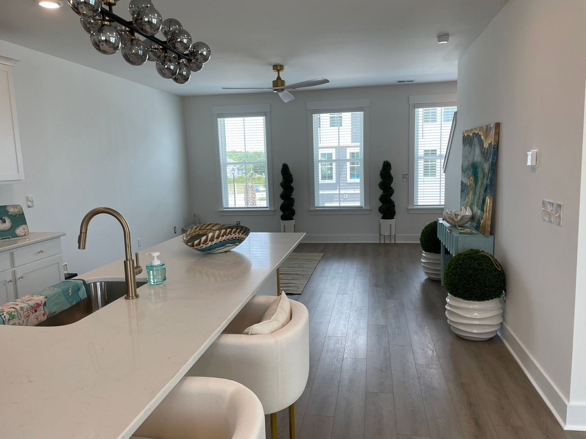 Bright modern kitchen with white island, wood floors, and large windows overlooking a living area