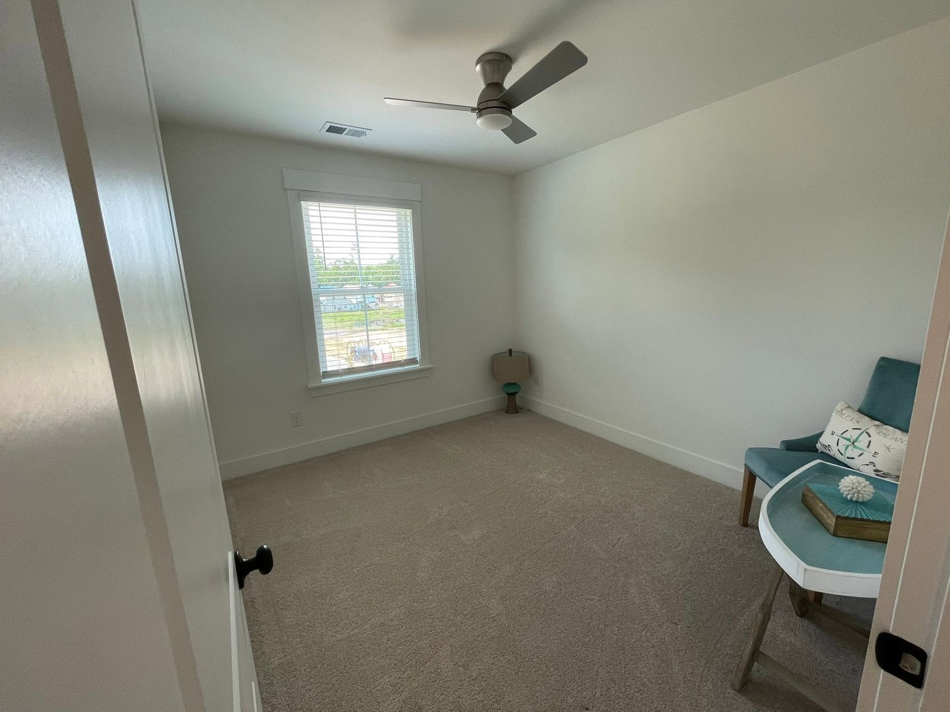 Empty carpeted bedroom with a ceiling fan, window, and a teal chair in the corner