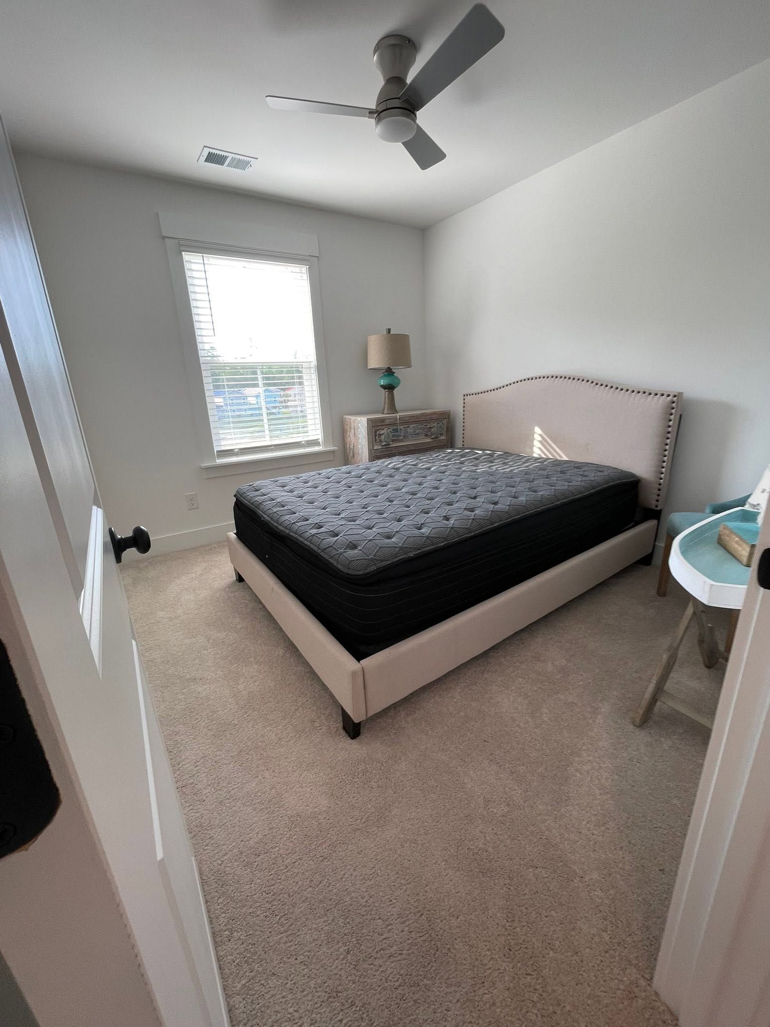 Bright bedroom with a bed, window, ceiling fan, dresser, and carpeted floor.