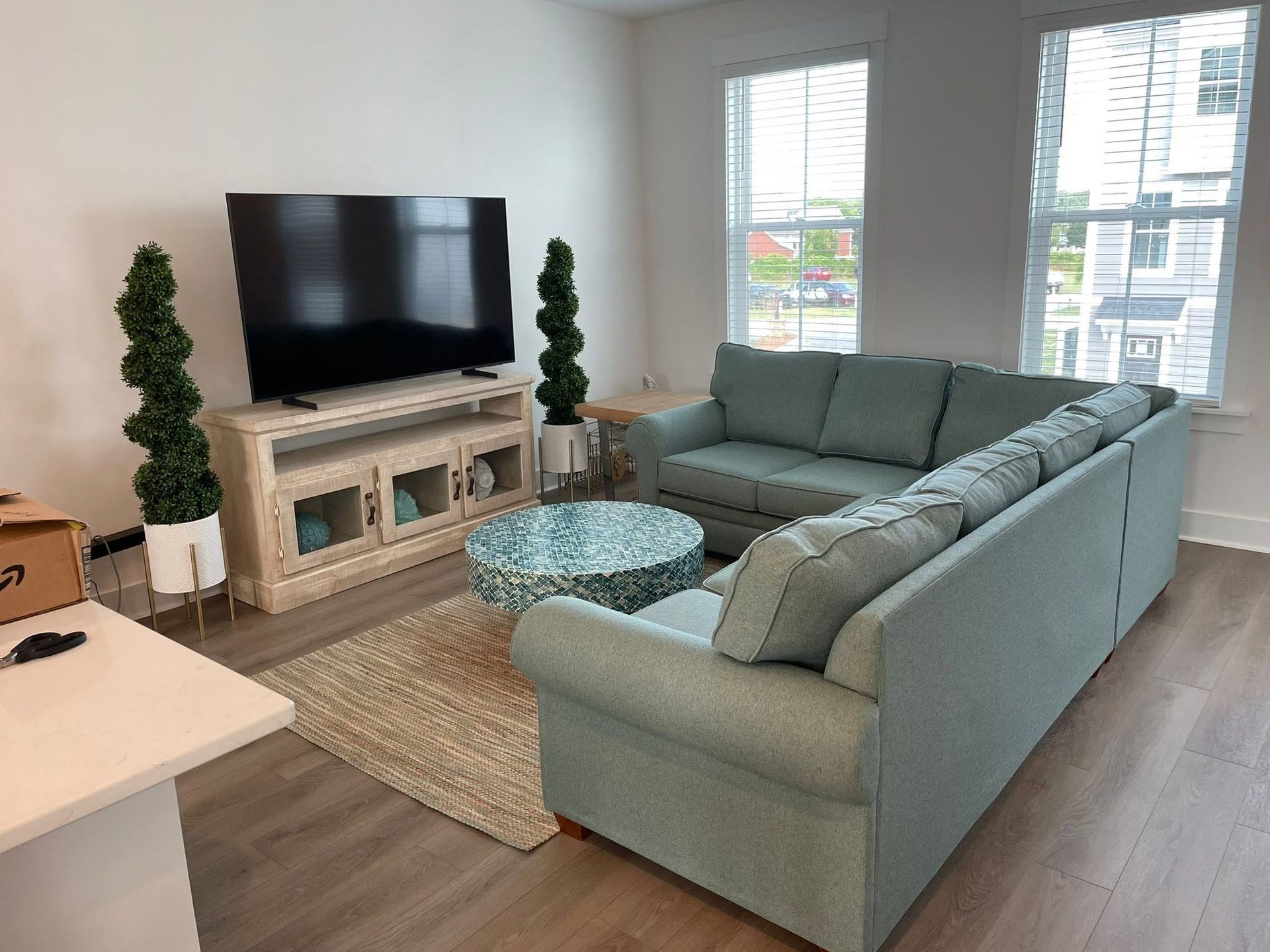 Bright living room with gray sectional, TV, fireplace, glass coffee table, and large windows