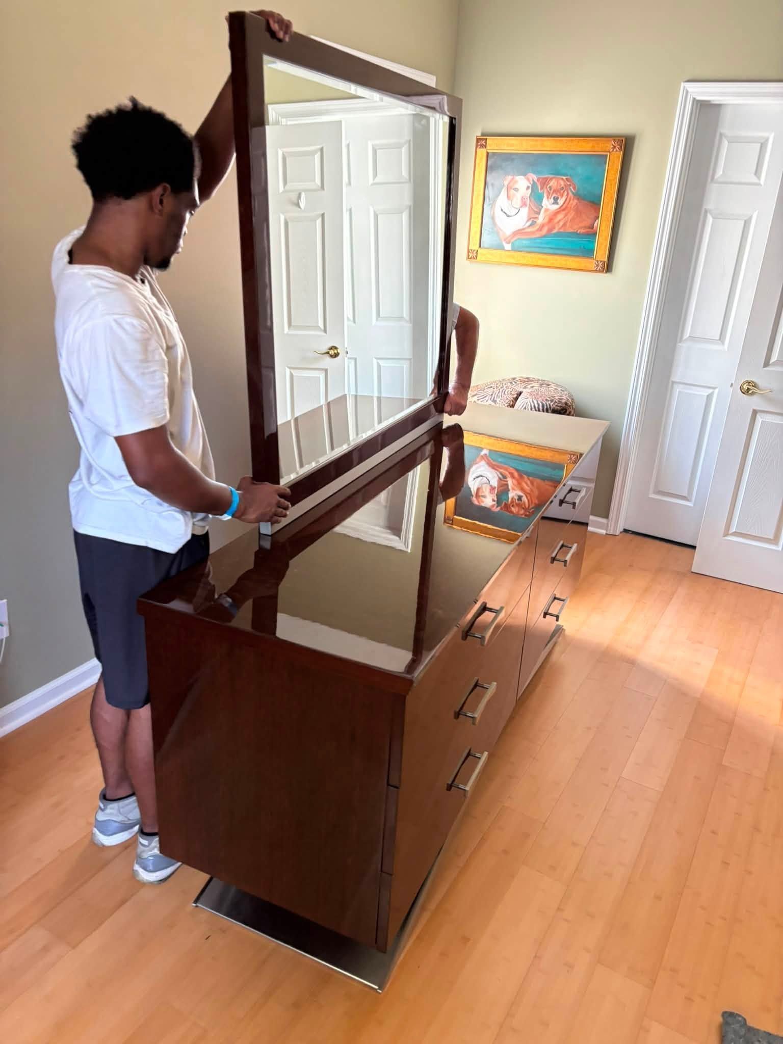 Person assembling a wooden dresser in a room with a mirror and painting on the wall