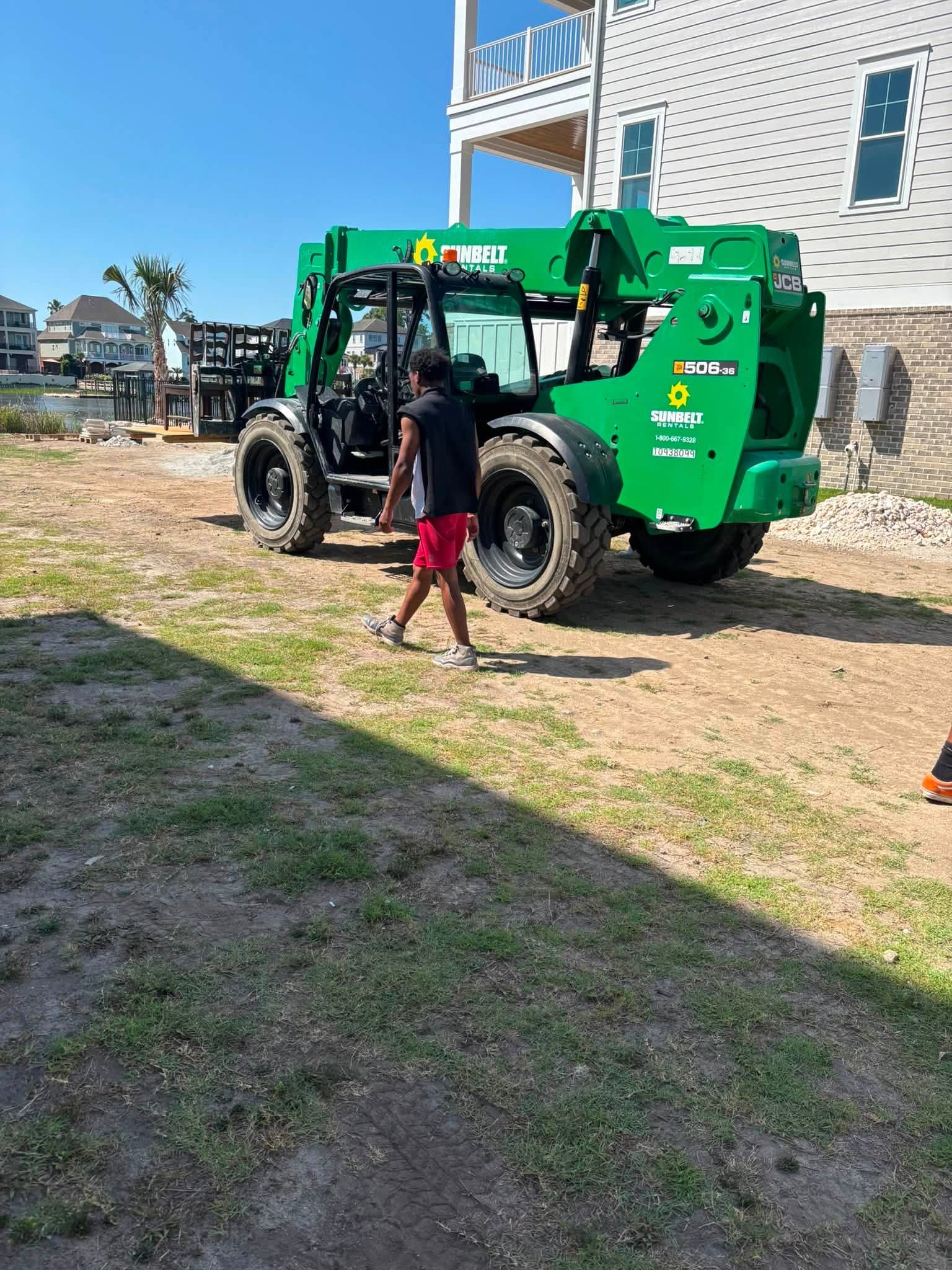 Child walking beside a green lift truck parked by a white house on a sunny day
