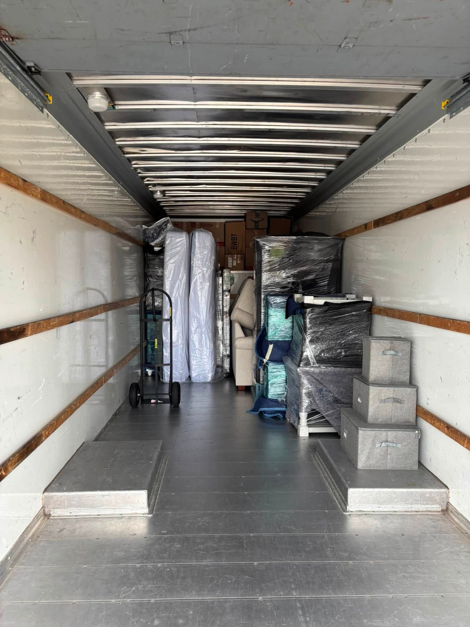 Inside a moving truck, packed boxes and wrapped furniture line the walls and floor.