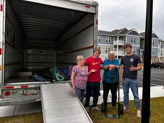 Four people stand beside a moving truck loaded with belongings on a residential street.