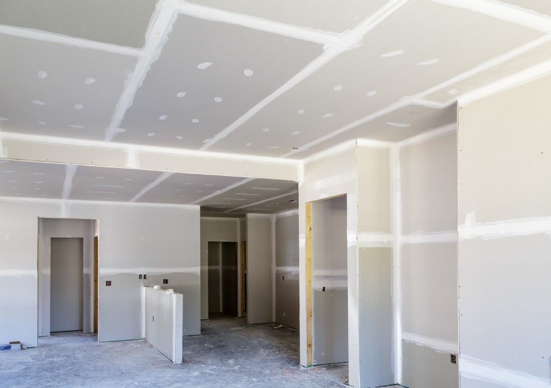 Interior room under construction, with drywall installed on walls and ceiling; taped seams are visible.