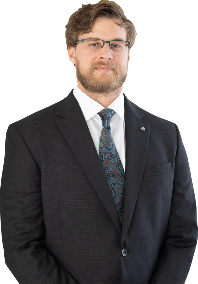 A professional headshot of a person with a beard, wearing a dark suit, white shirt, and patterned tie against a white background.