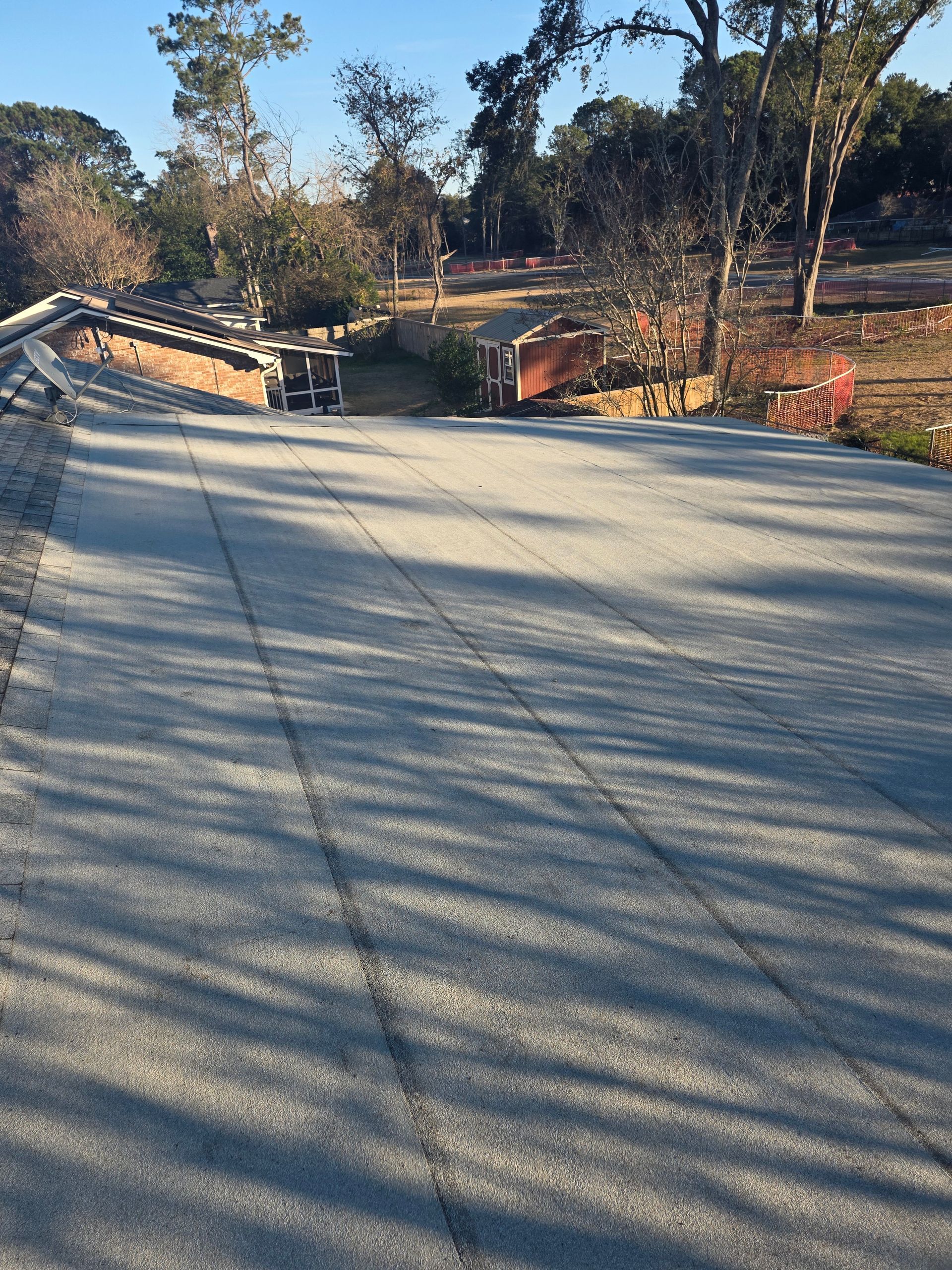 Curved road with long tree shadows, orange construction barriers, and wooded hillsides in daylight
