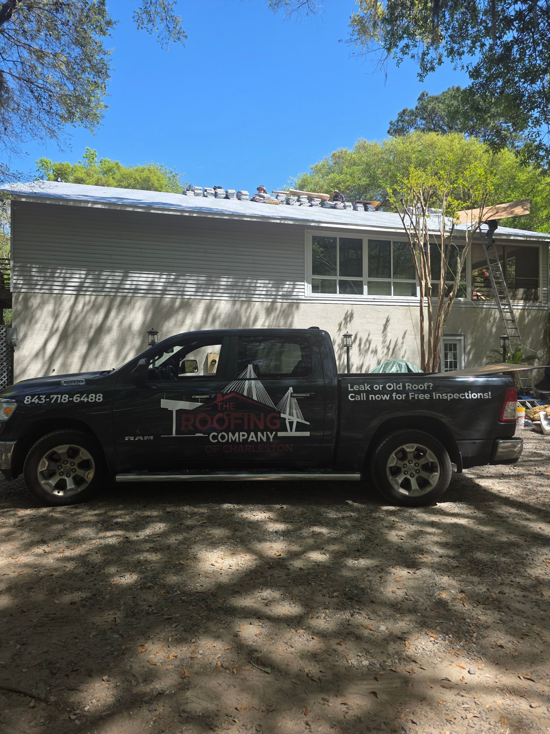 Black pickup truck parked in front of a gray house under trees on a sunny day