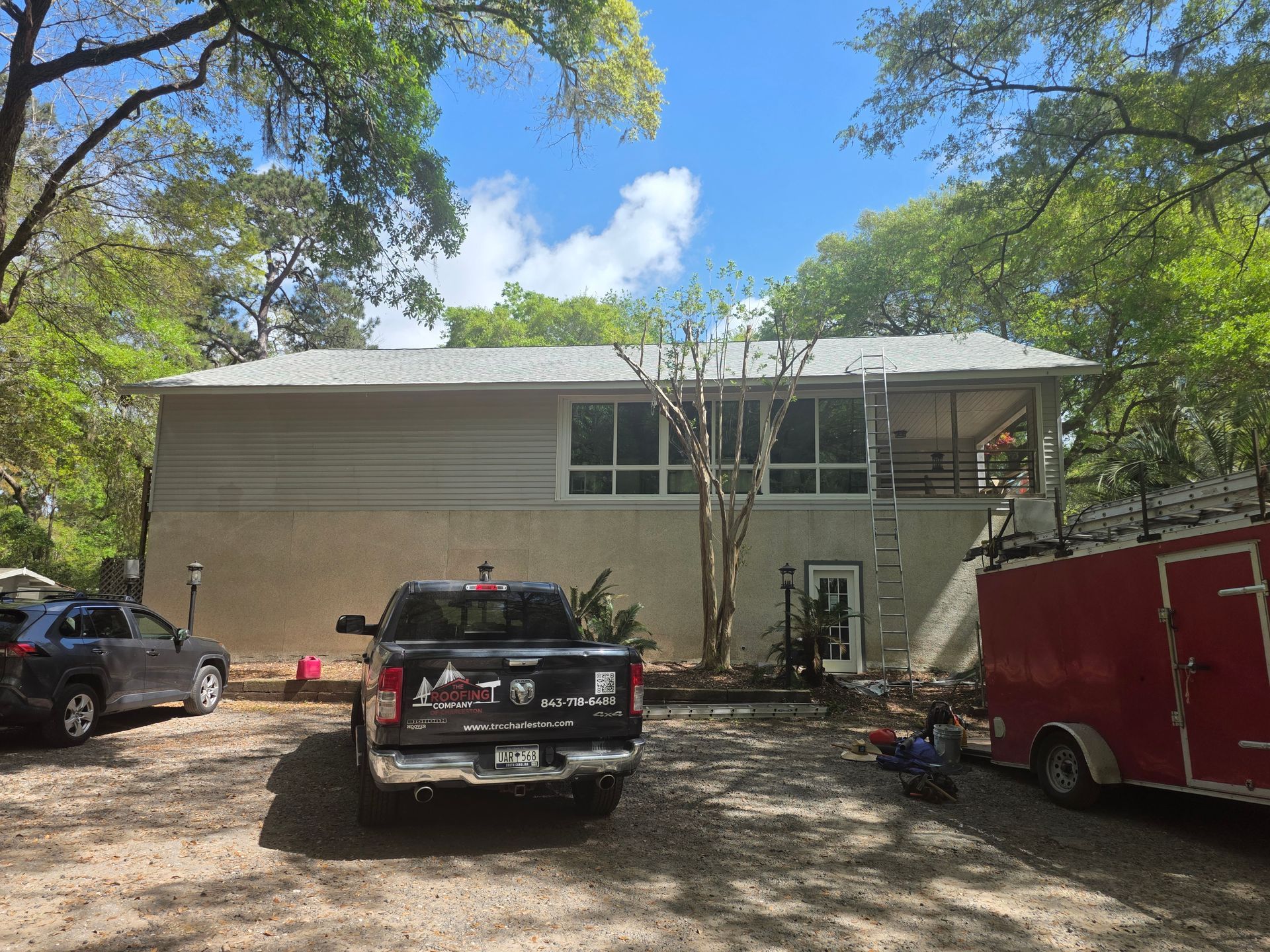 Two-story beige house with trucks parked in front under trees