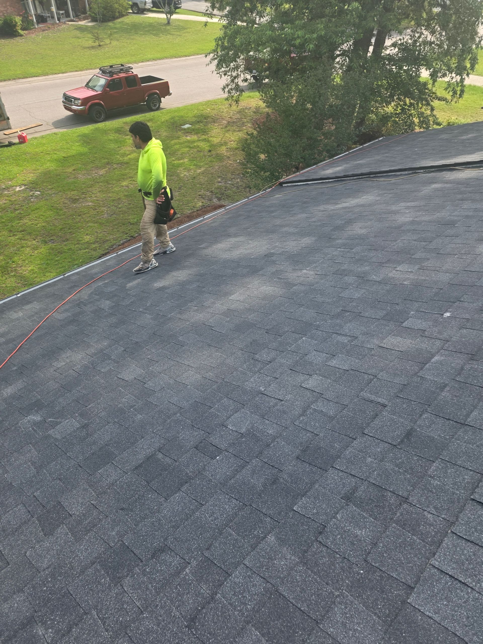 Worker in a neon shirt using a power tool on a roof, with a street and parked car below.