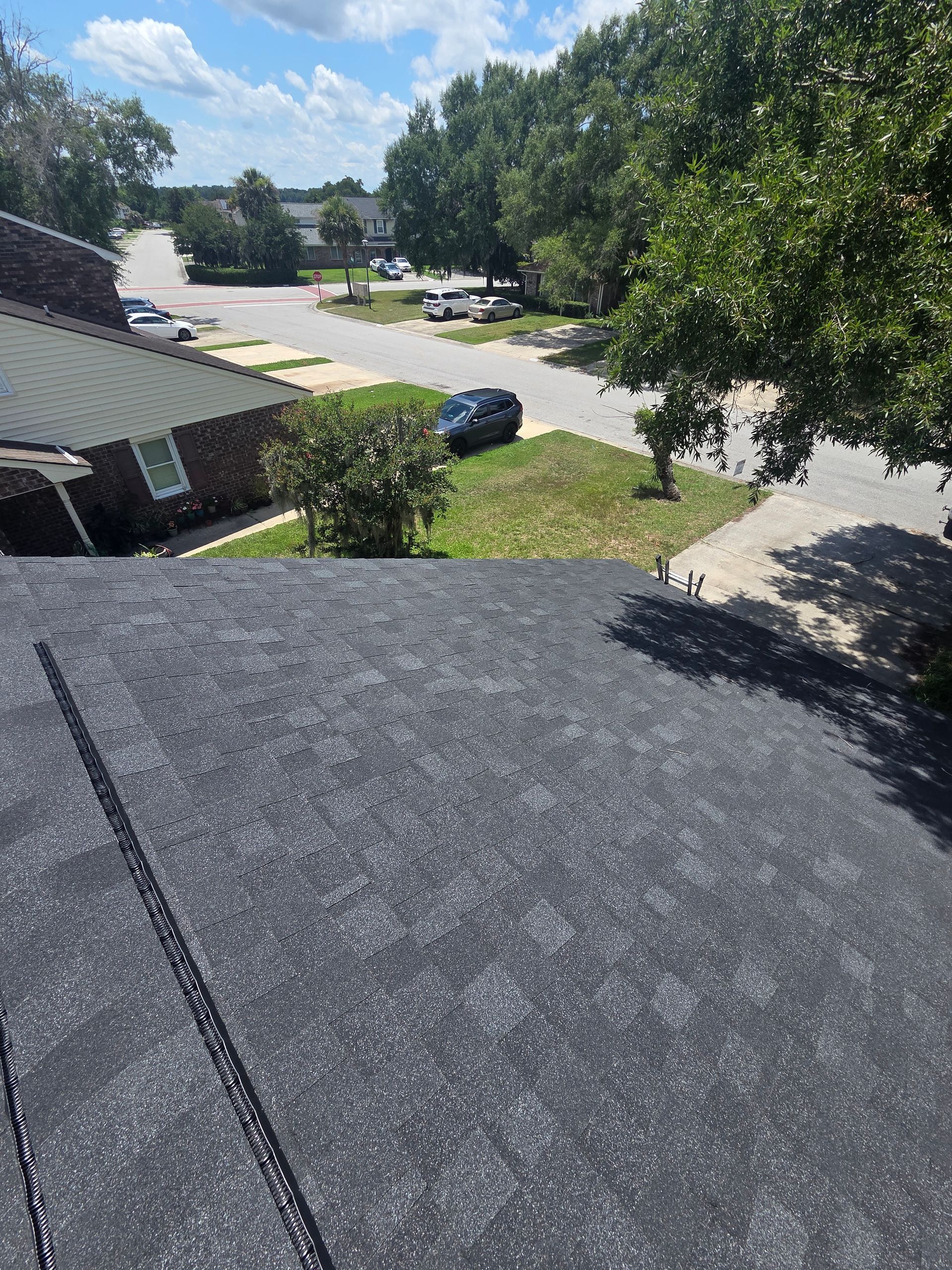 Rooftop view of a suburban street with trees, parked cars, and blue sky