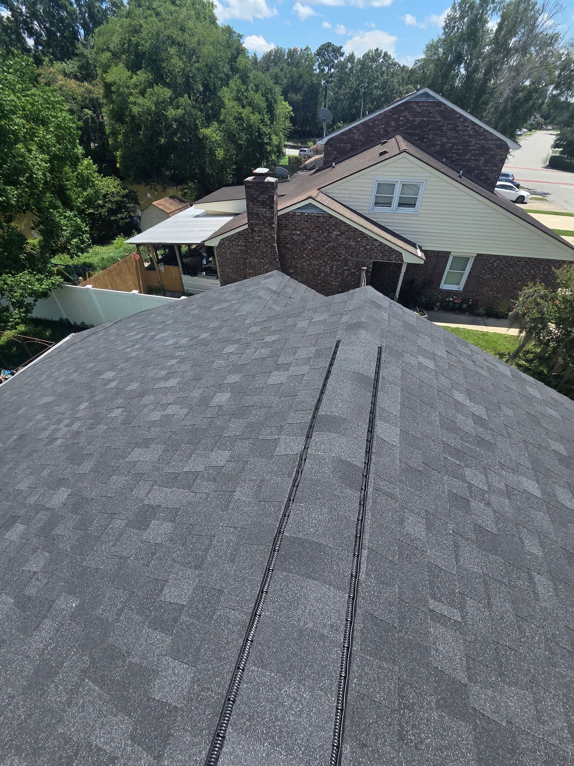 Rooftop with gray shingles and a brick chimney, overlooking houses and trees on a sunny day