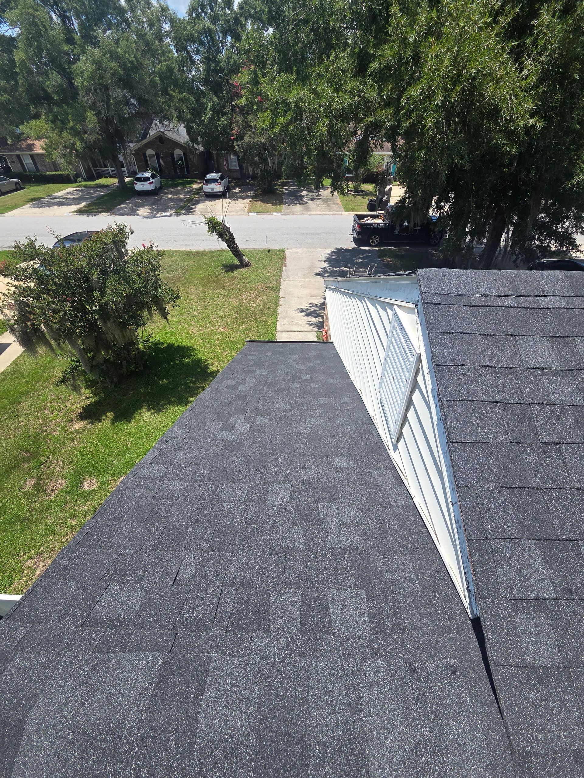 Rooftop view of gray shingles and white gutter beside a tree-lined residential street.
