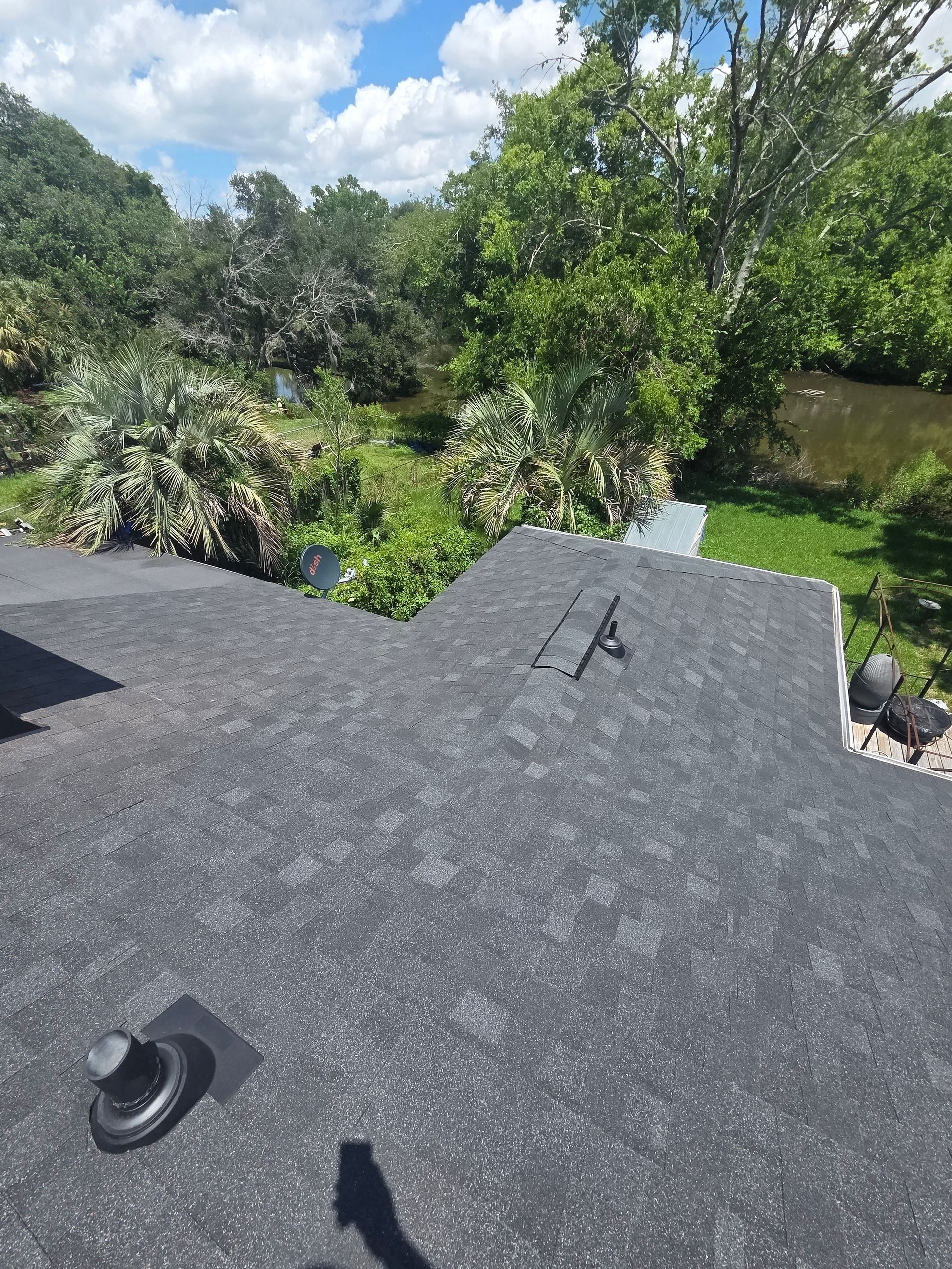 Roof edge overlooking a green backyard and trees under a cloudy sky