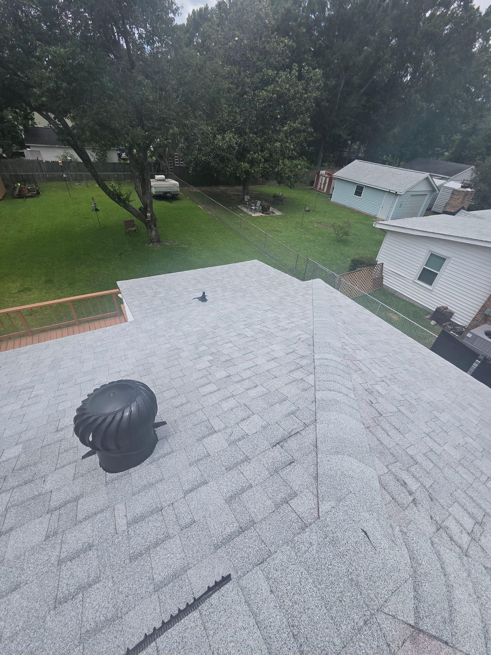 Rainy rooftop and yard view with a black vent and white house under overcast sky