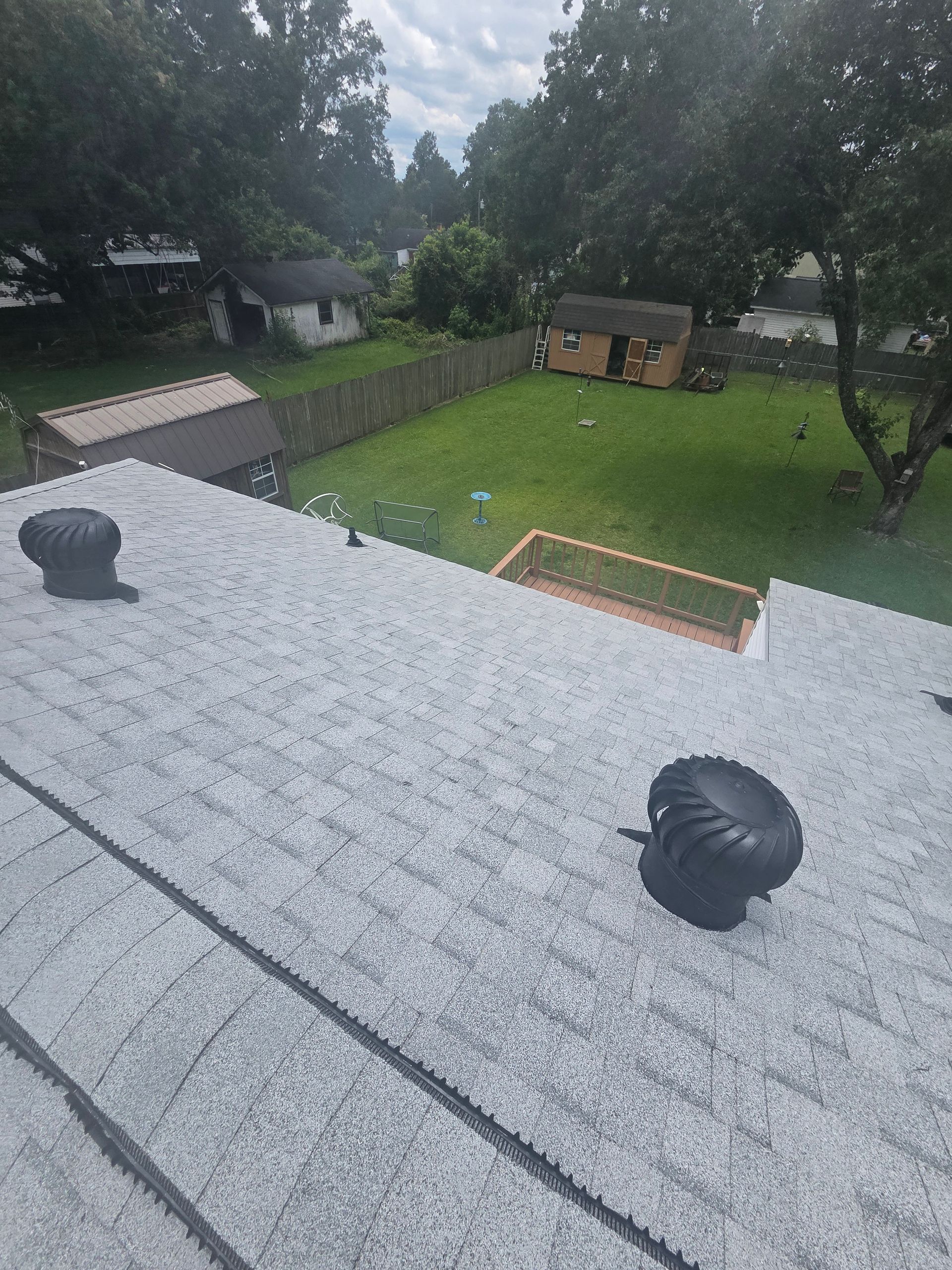 View from a roof over a backyard with green lawn, trees, shed, and small play structure on a rainy day