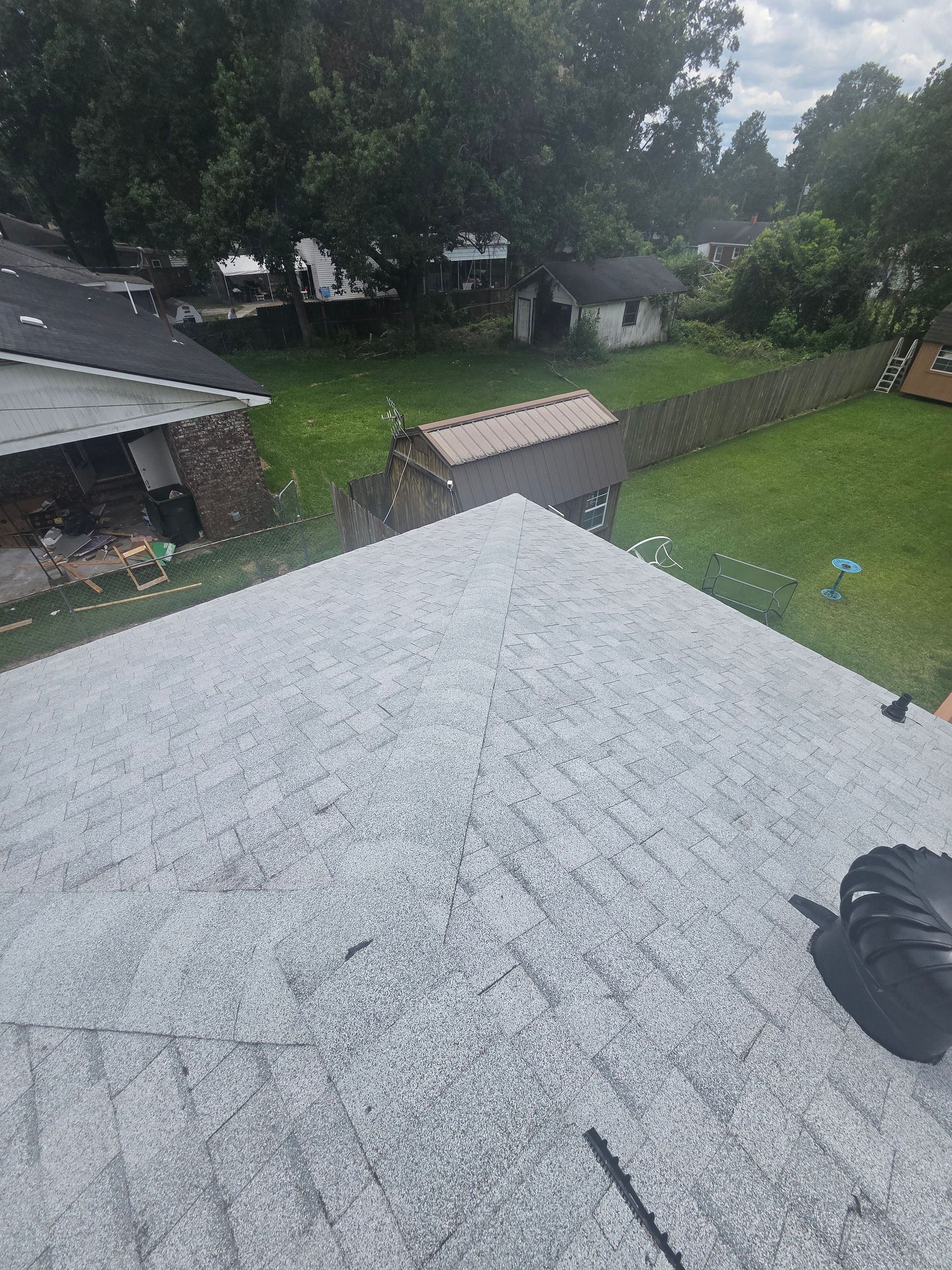 Rooftop view over a rainy backyard with trees, sheds, and a lawn; a gloved hand is visible at the edge.