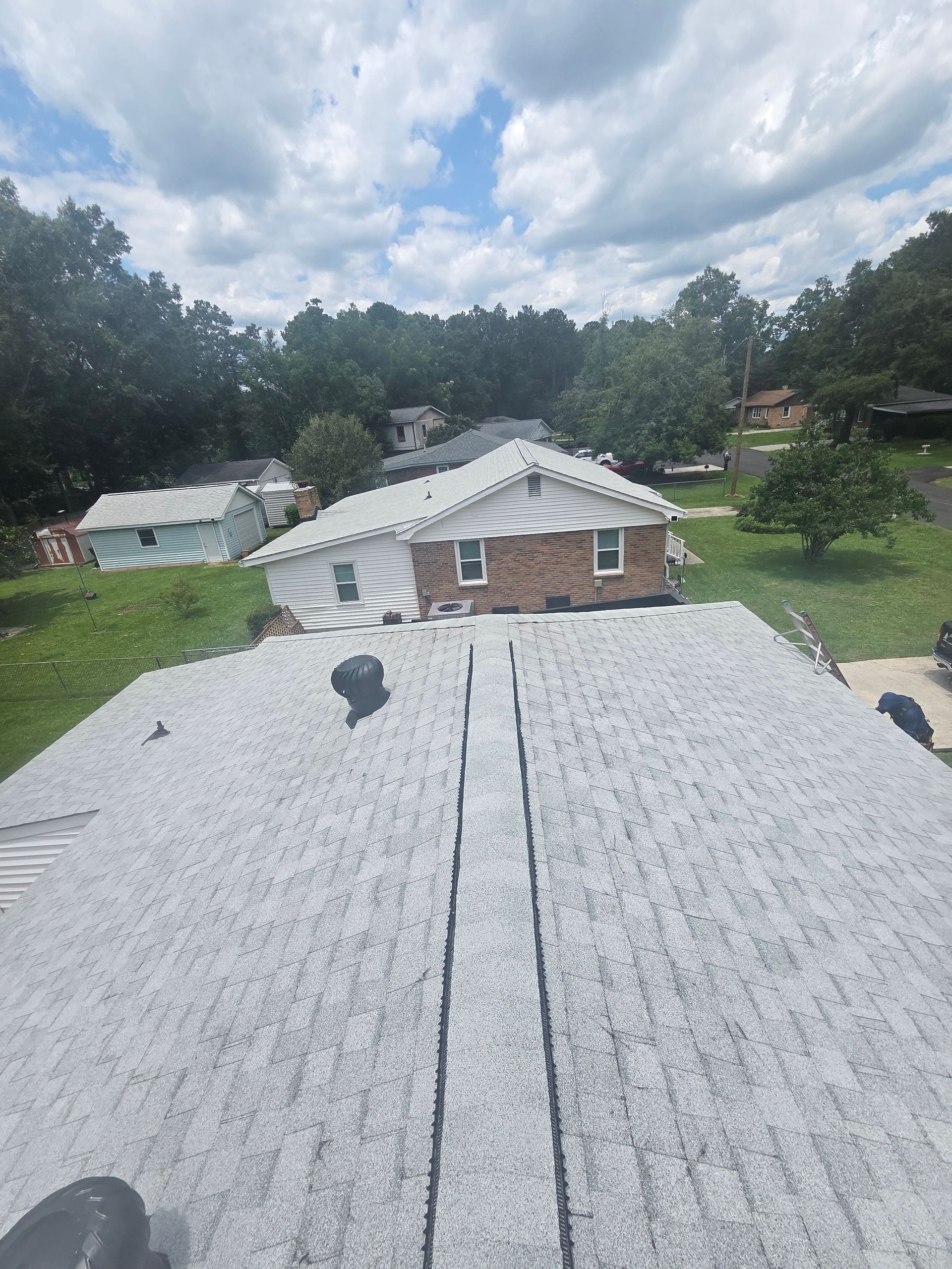 View from a roof over a suburban house and trees under a cloudy sky