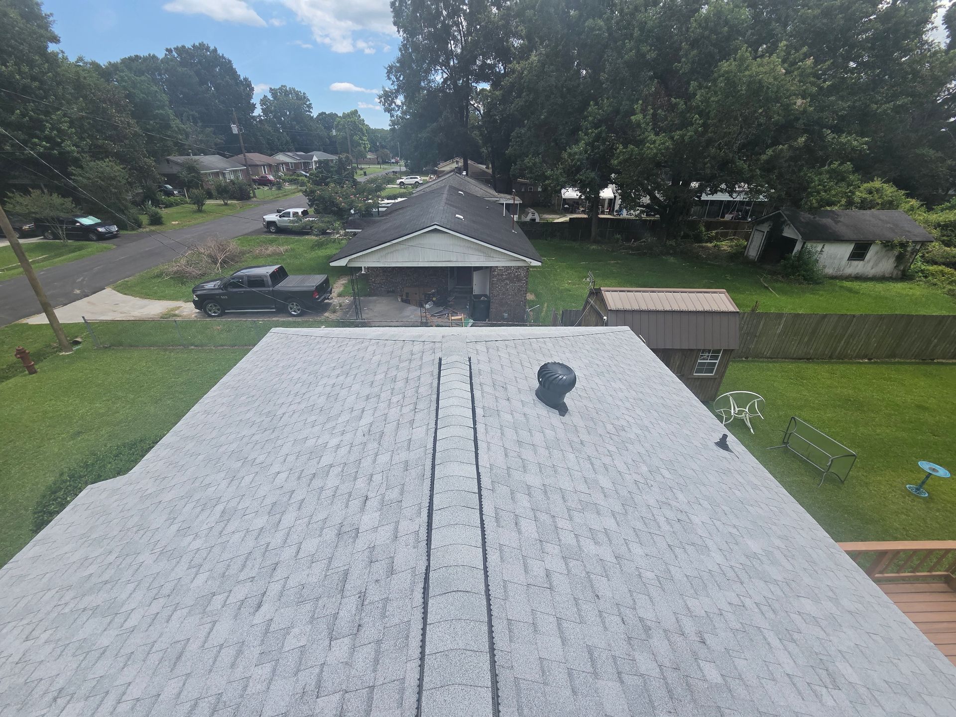 Rooftop view over a suburban neighborhood with trees, houses, and a partly cloudy sky