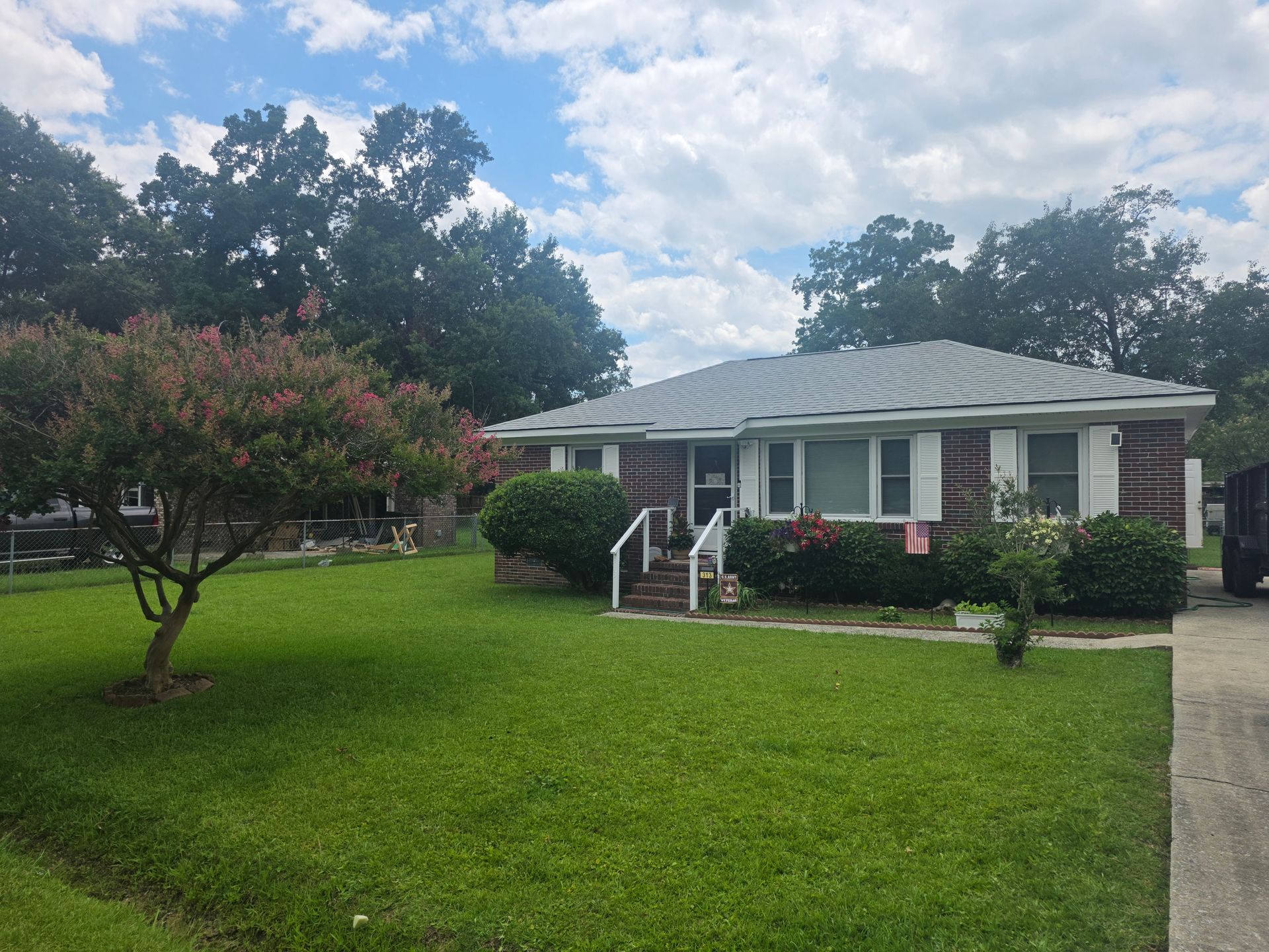 Single-story brick house with white trim, a green lawn, and flowering trees under a cloudy sky