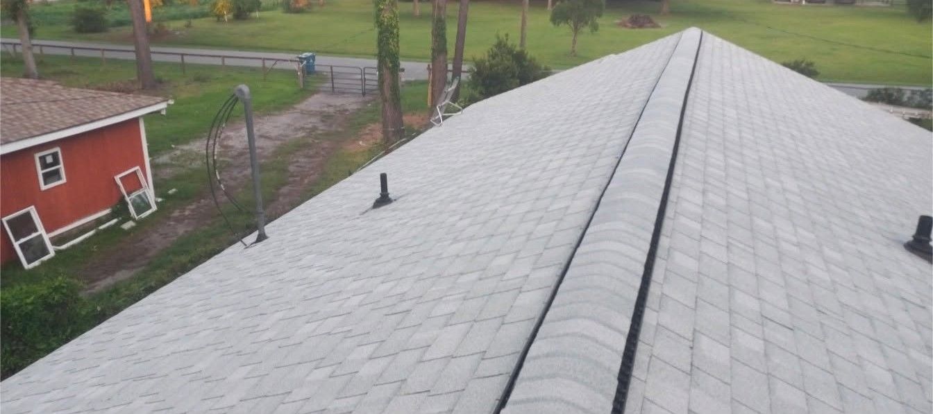 Rooftop shingles leading toward a red barn and green yard on an overcast day.
