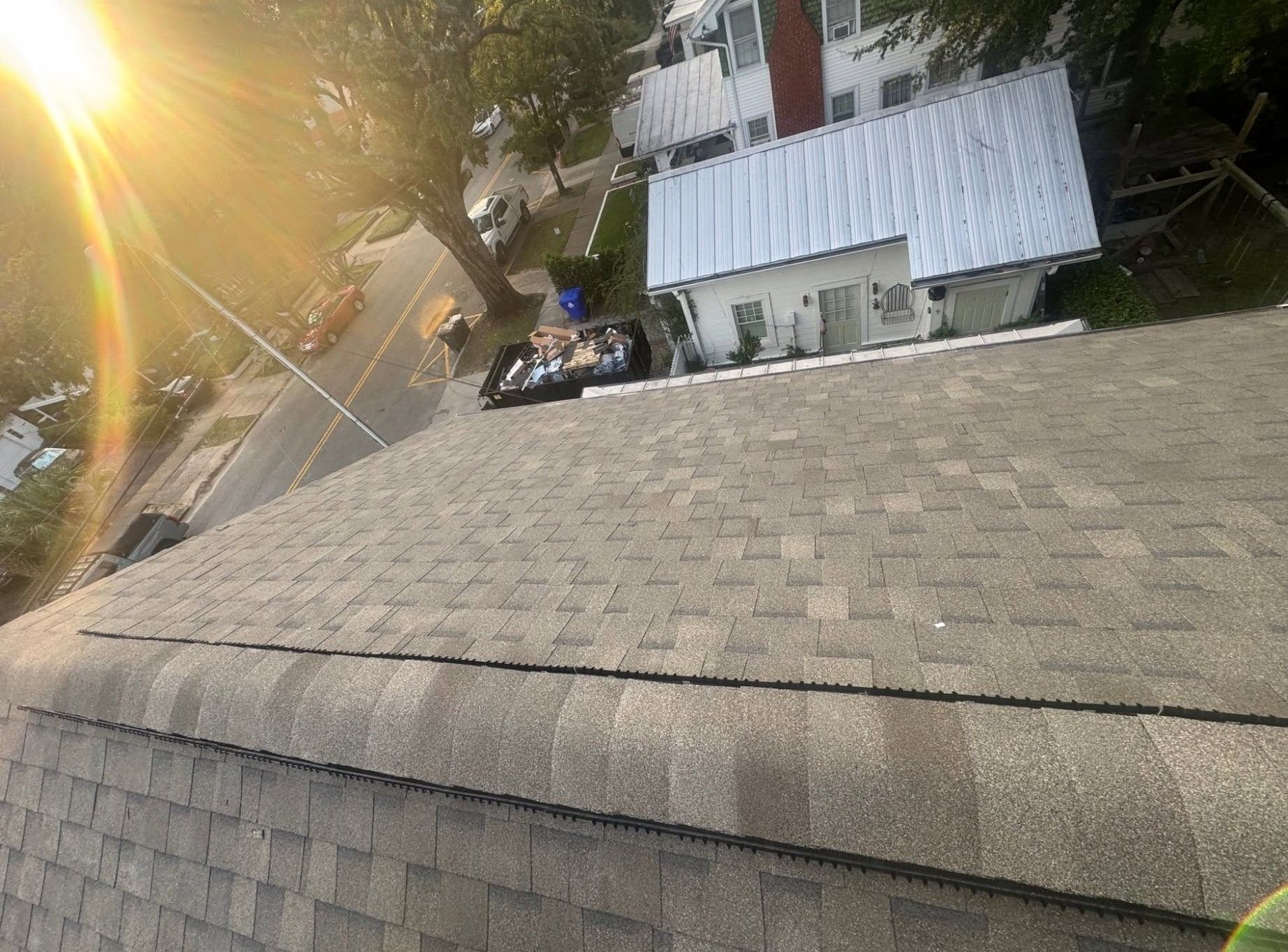 Tilted rooftop with a small white building and trees in warm sunlight