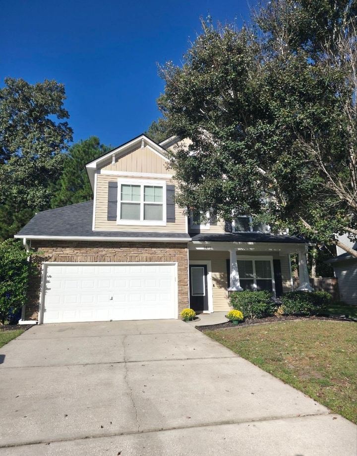 Two-story beige house with white garage and driveway, shaded by large trees