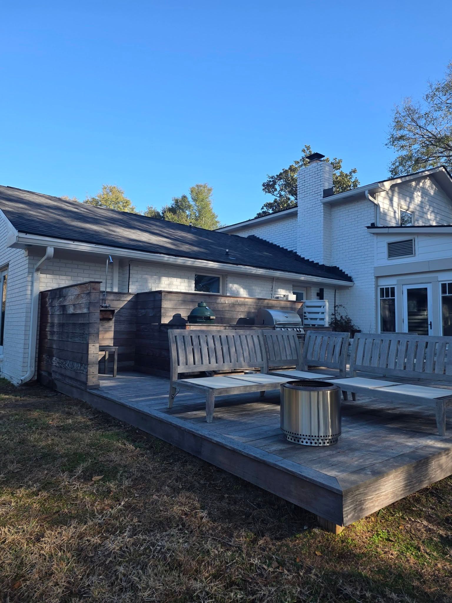 White house patio with wooden benches, a fire pit, and a clear blue sky