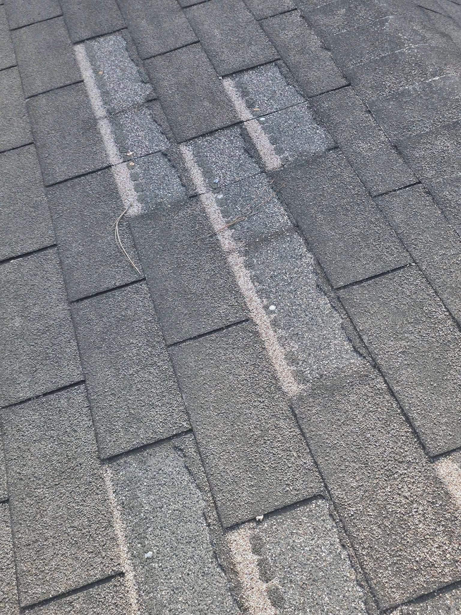 Close-up of gray asphalt shingles with a white streak running diagonally across the roof.