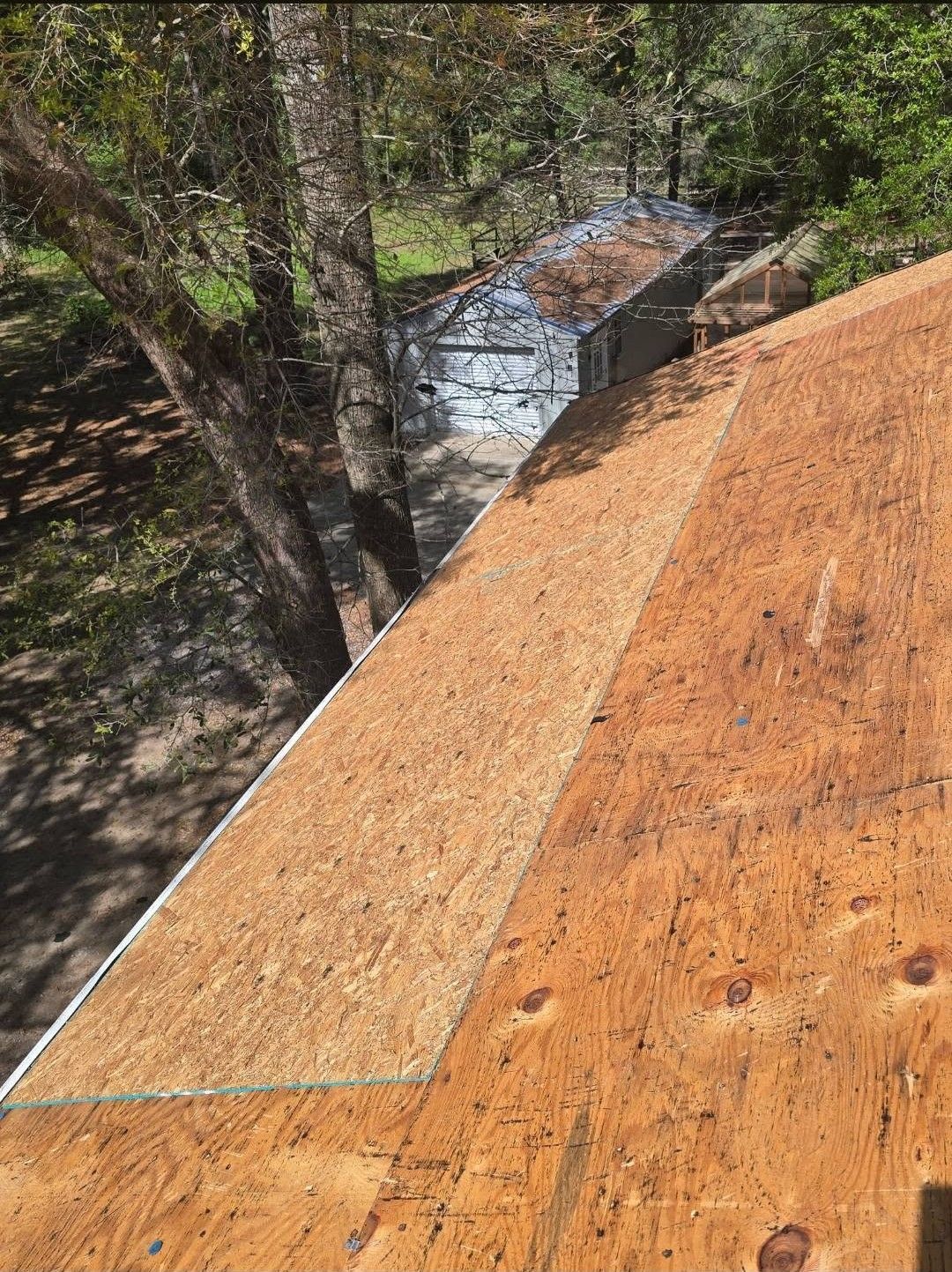 Wooden roof under construction beside trees, with a stream visible below.